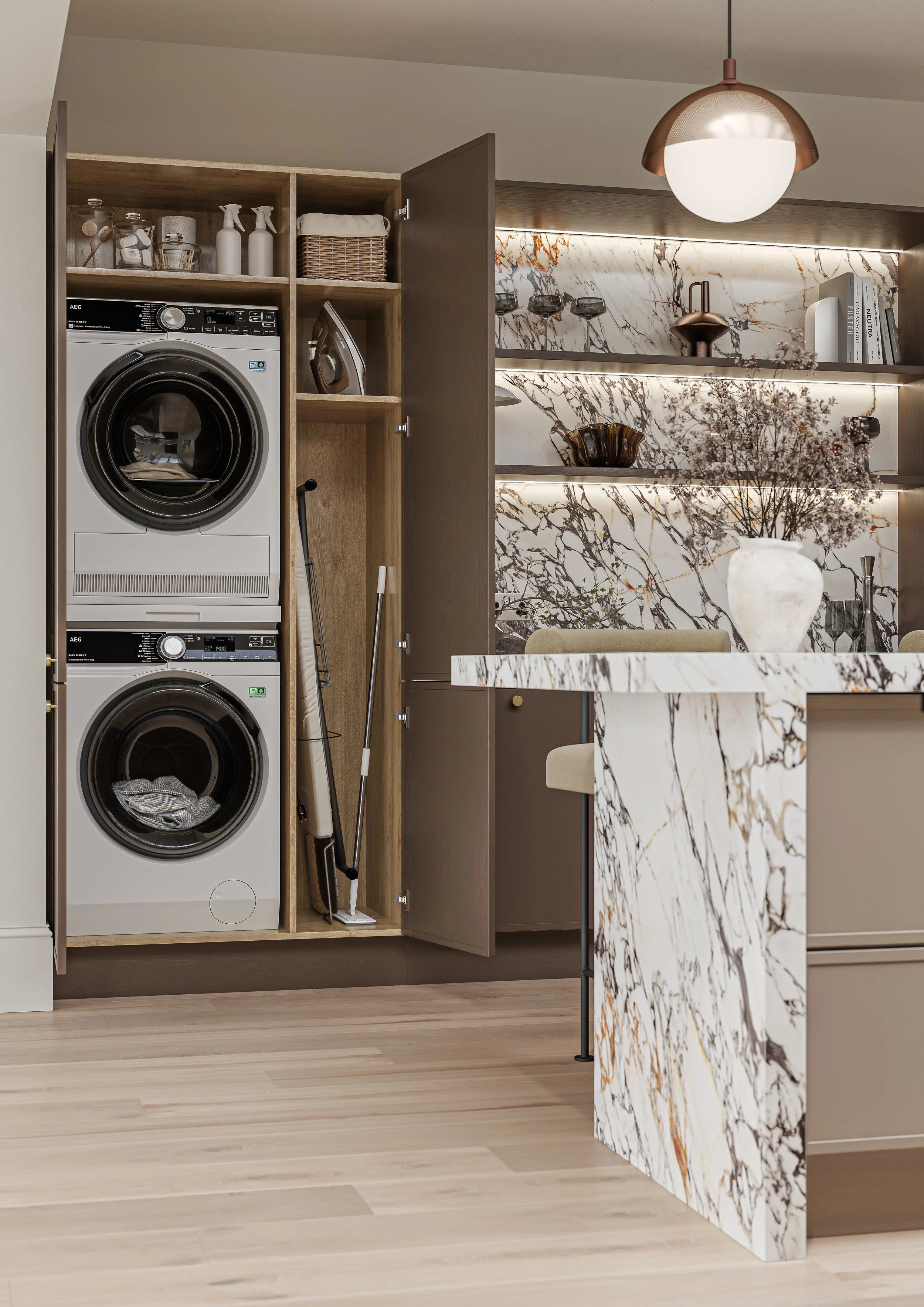Hidden Utility Unit in a modern brown kitchen housing a washing machine, tumble dryer, iron and ironing board along with cleaning products. Also featured in the kitchen is a striking quartz pattern, open shelving and a pendant light.