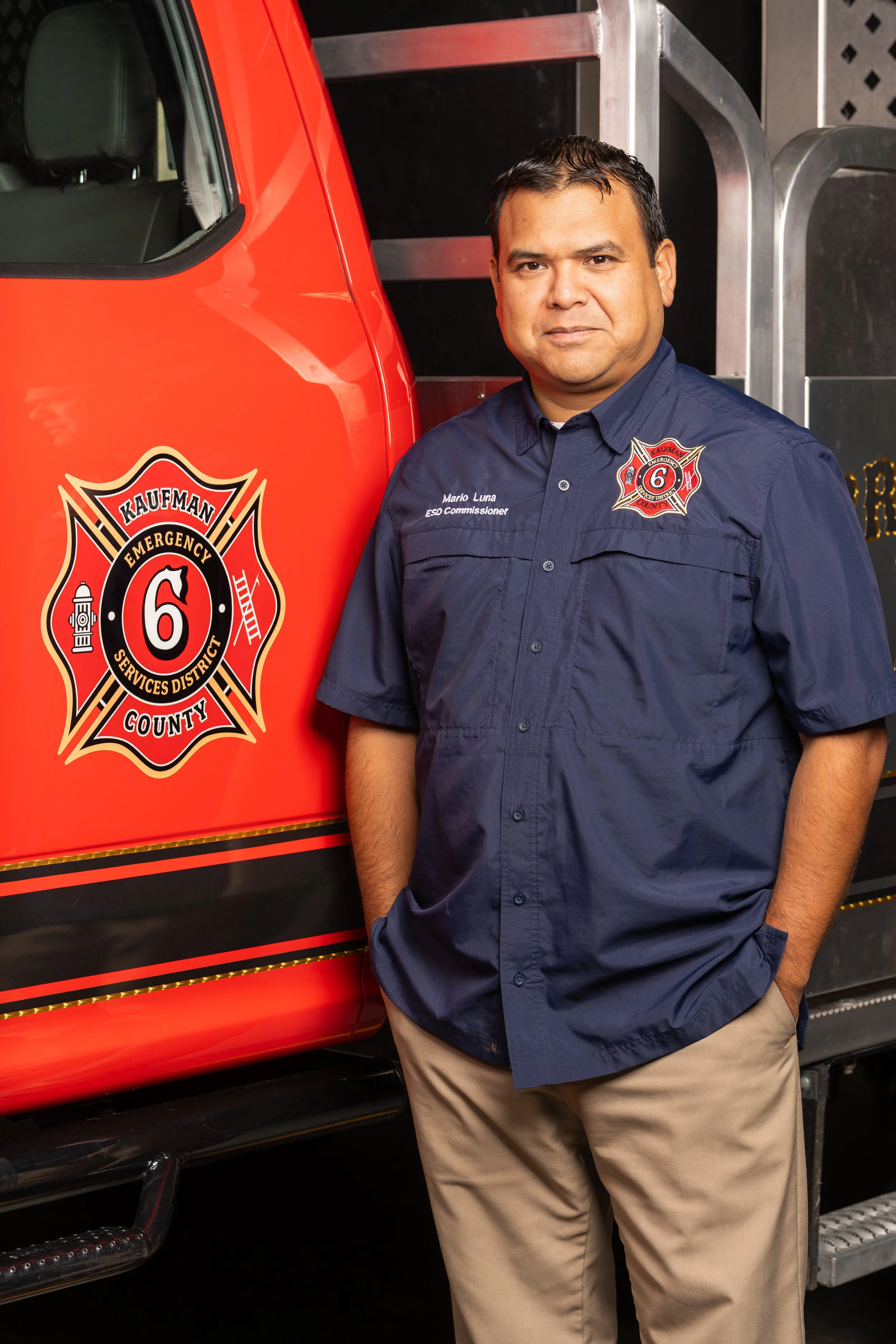 Headshot of a man in a gray suit with a light blue checkered shirt and a light blue and white diamond-patterned tie, wearing a lapel pin.
