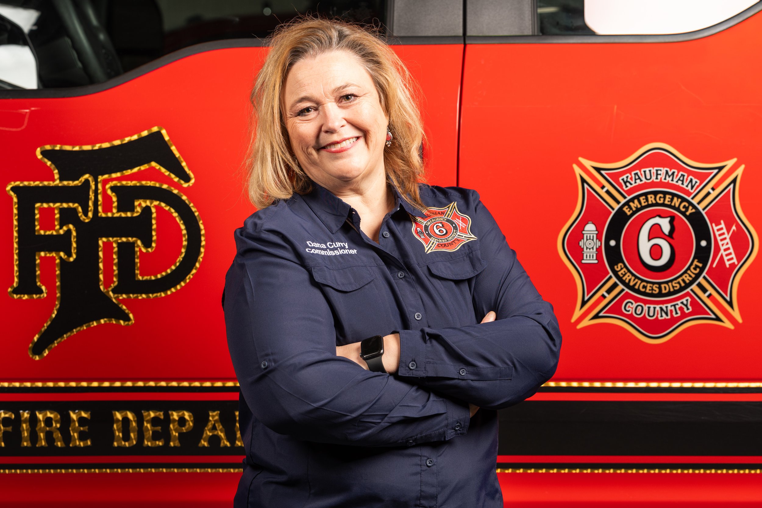 A woman with shoulder-length brown hair wearing a red top and earrings, smiling at the camera against a neutral background.