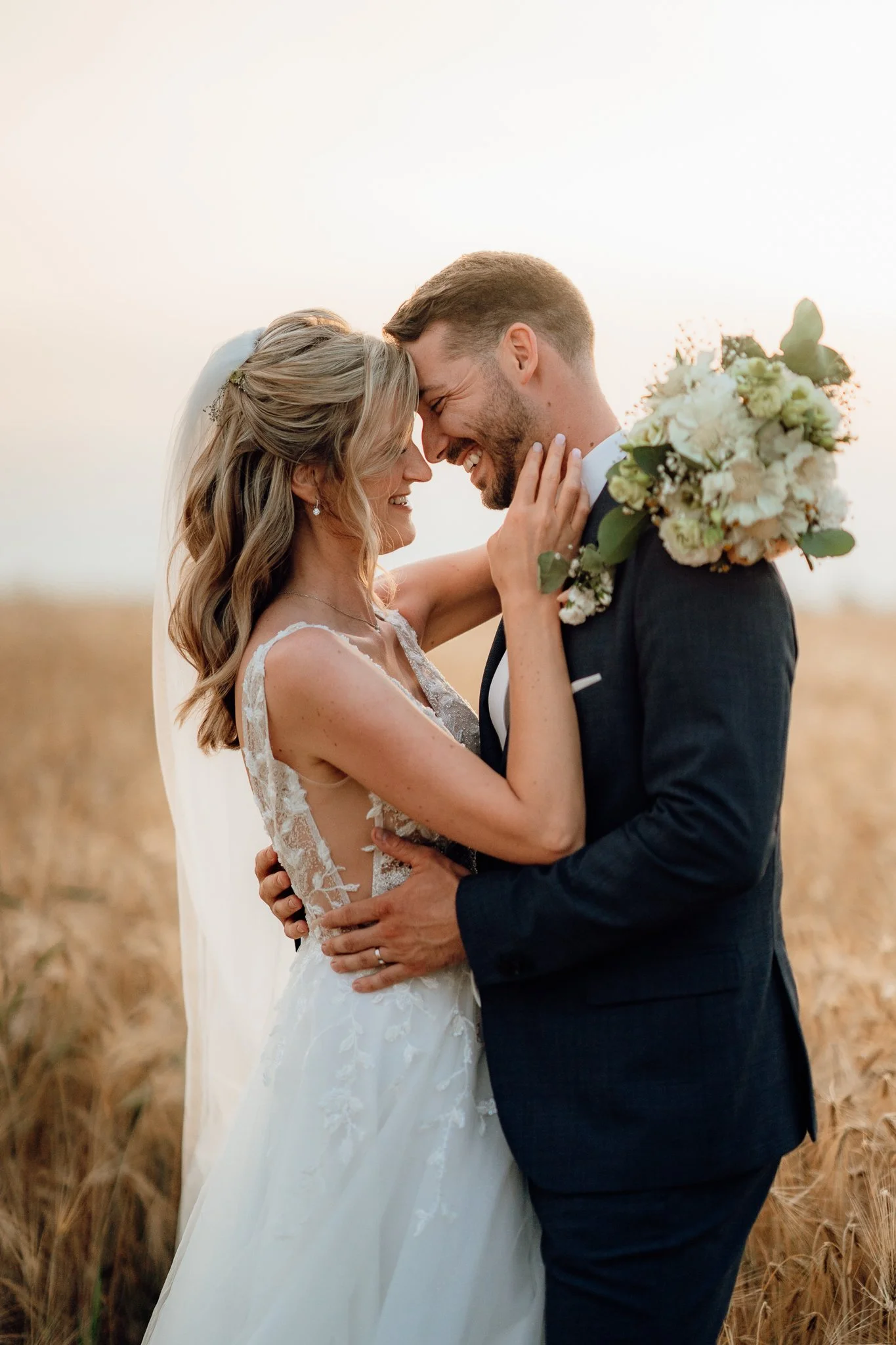 Nevěsta a ženich objímající se při západu slunce v poli - přirozená svatební fotografie od svatební fotografky z Brna.