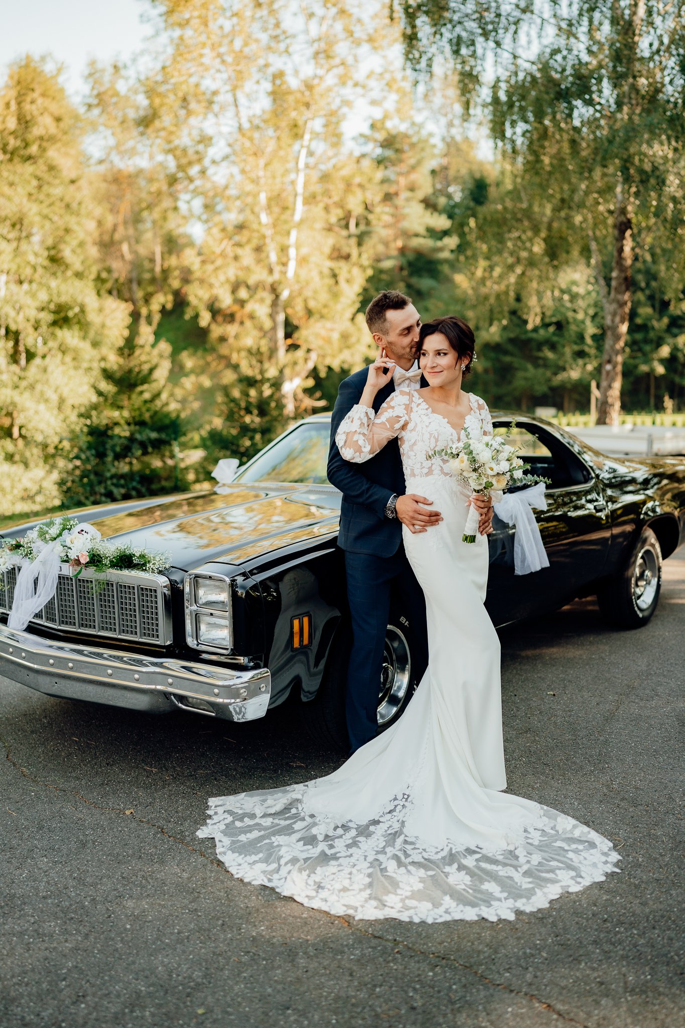 Elegantní póza nevěsty a ženicha u luxusního automobilu. Krásná barevná svatební fotografie. 