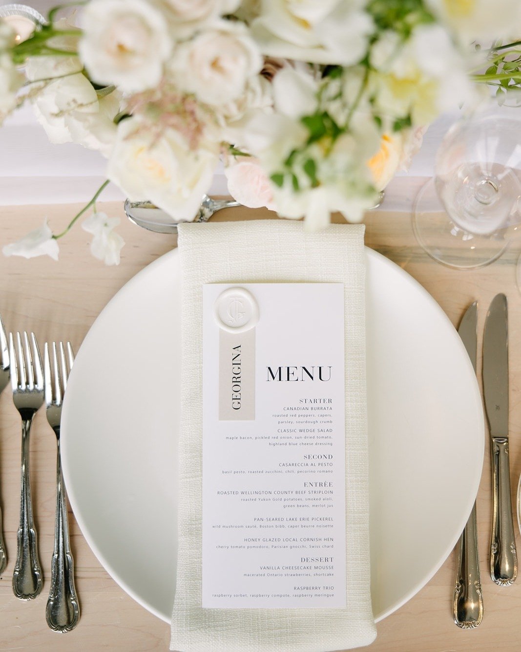 A classic white wedding place setting never goes out of style! Julia and Gavin's elegant tablescape featured a smooth modern charger plate layered with a textured napkin, crisp white menu, and a neutral taupe place card. Set atop a whitewashed table,