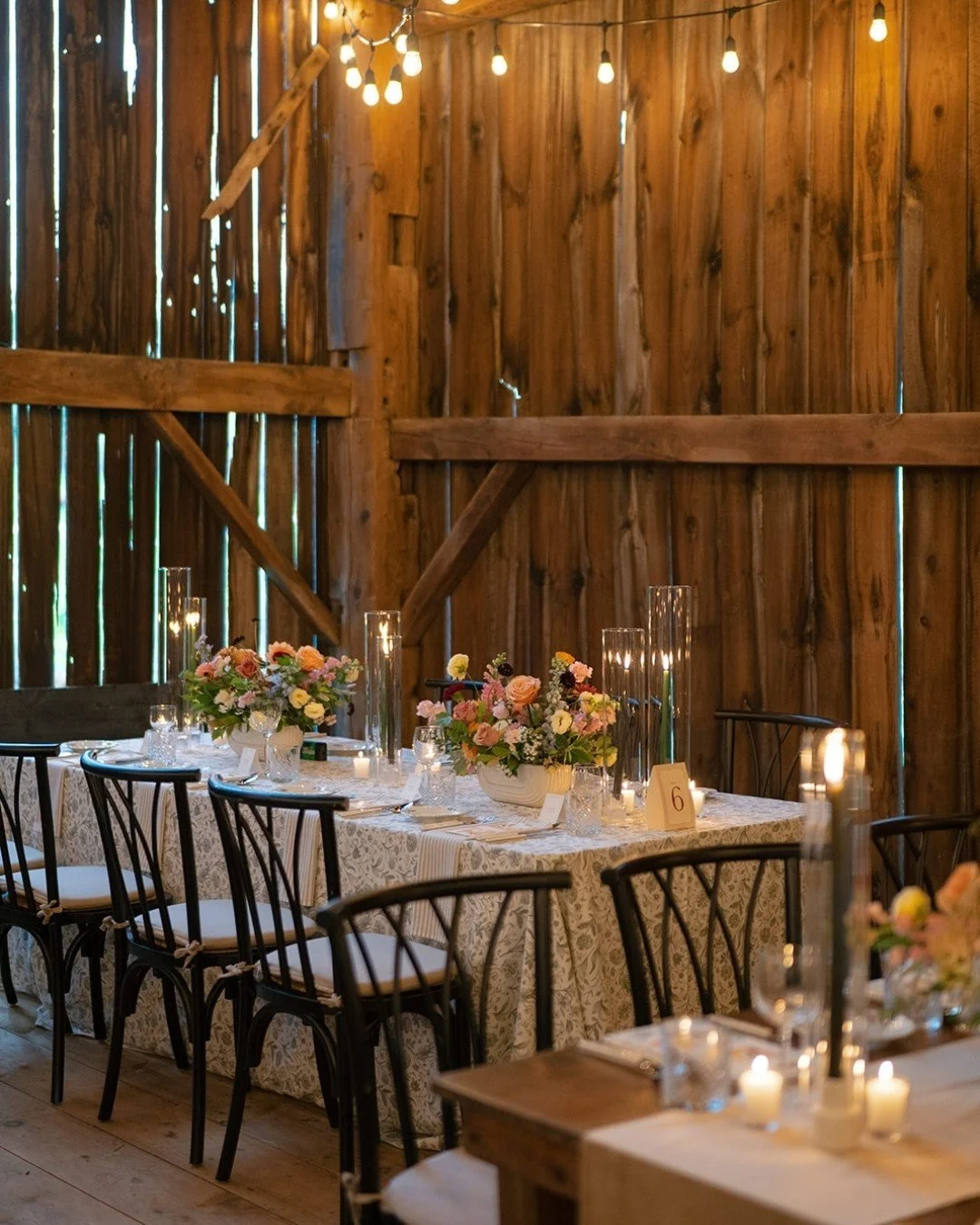 Honoring the barn&rsquo;s rustic charm while adding refined details was the goal. Raw wood, harvest tables, and agricultural elements paired with ochre velvet runners, soft patterned linens, and warm candlelight created a space that felt cozy, elegan