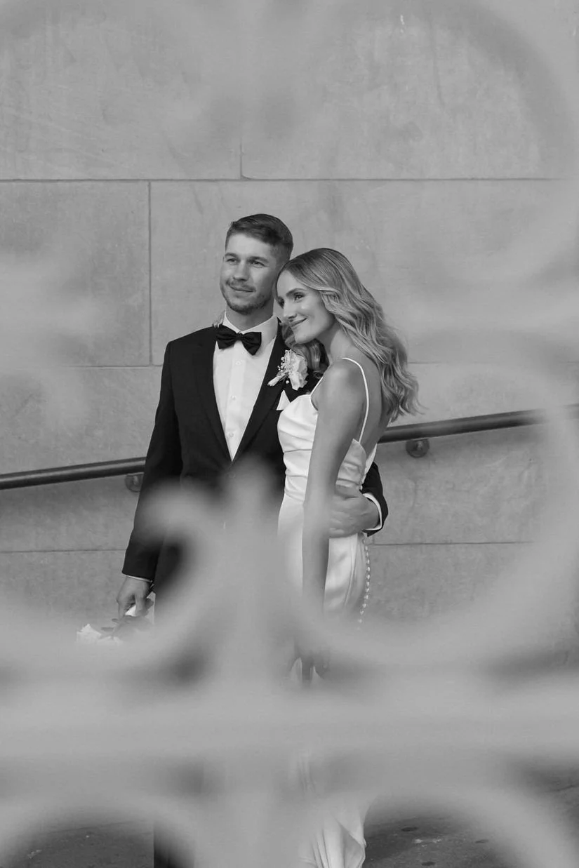 A black and white photograph of a bride and groom in front of a stone wall.