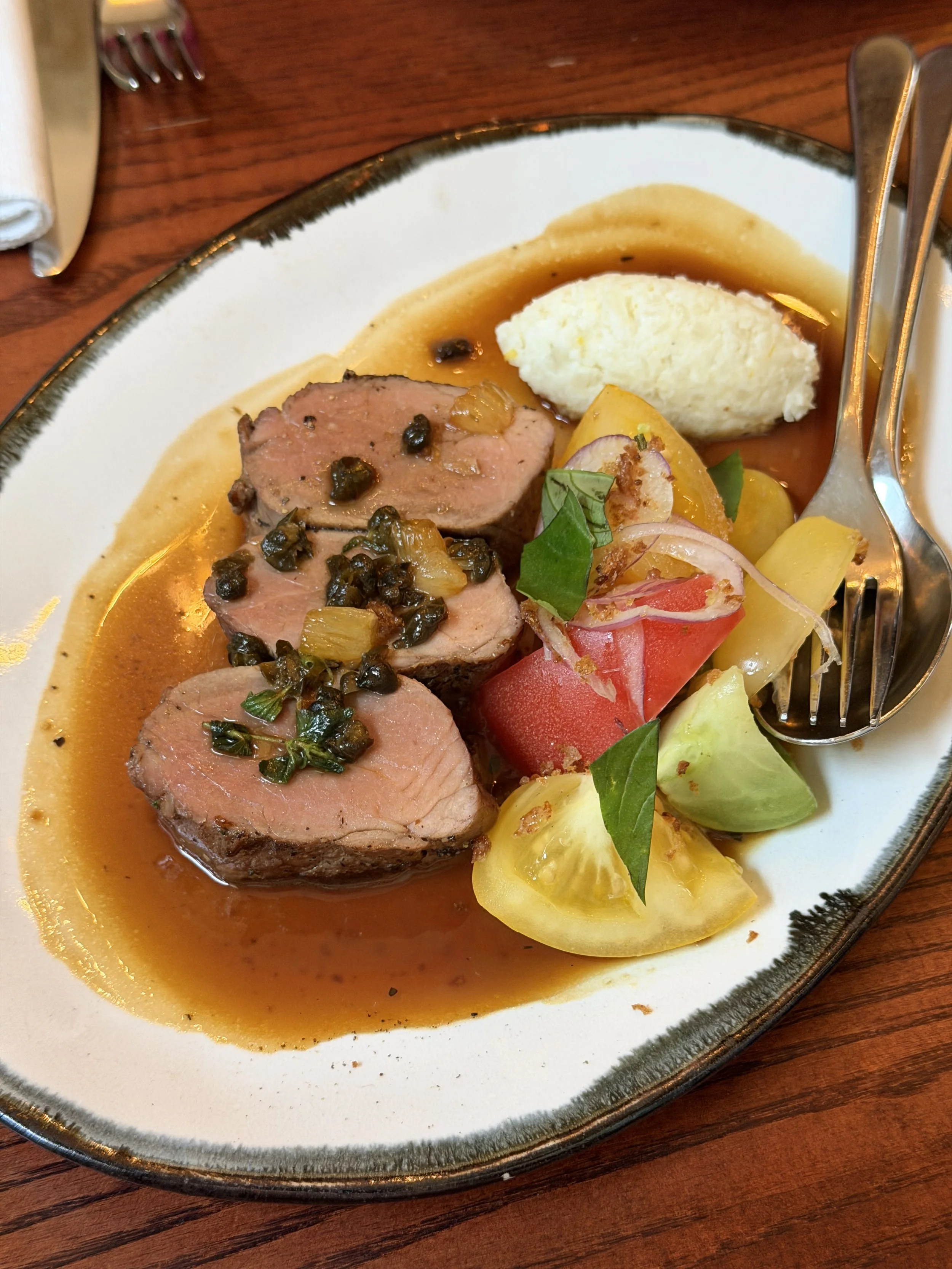 Iberico Pork with Tomato & Tropea Onion Salad and Lemon & Caper Sauce on a serving dish