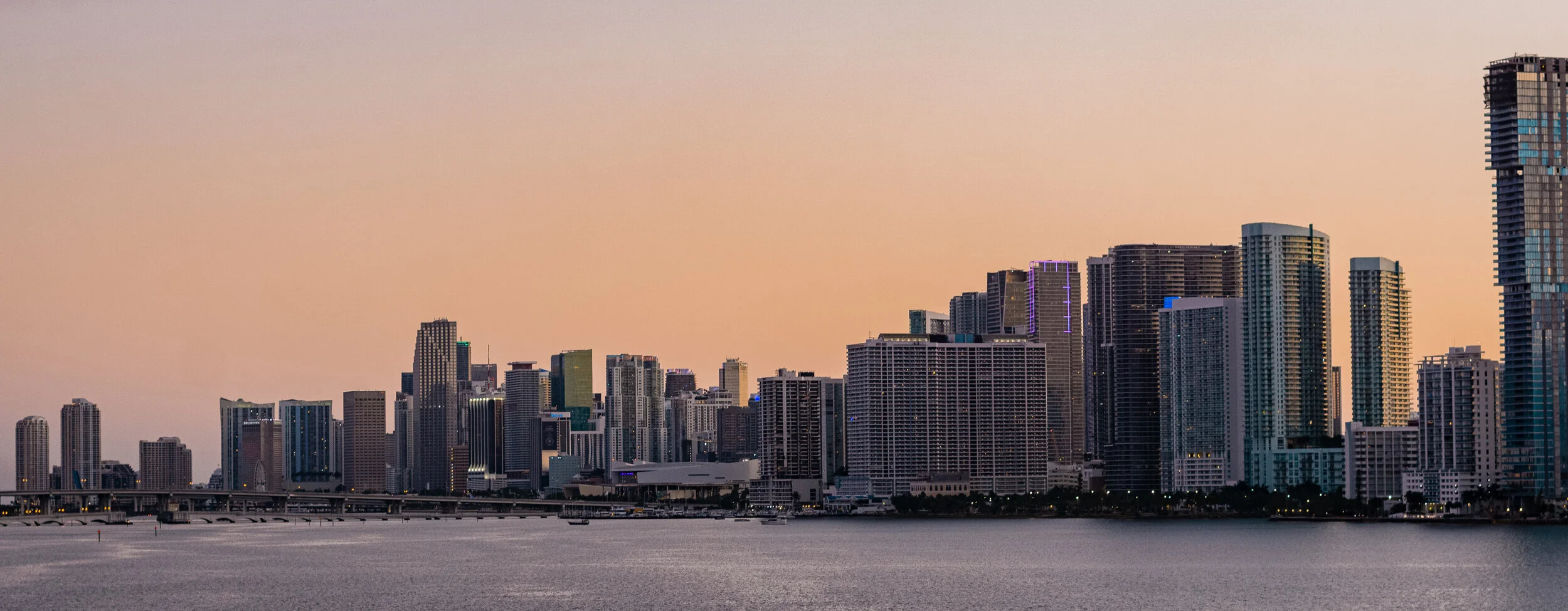 Skyline of Miami with high-rise buildings at sunset over the water.