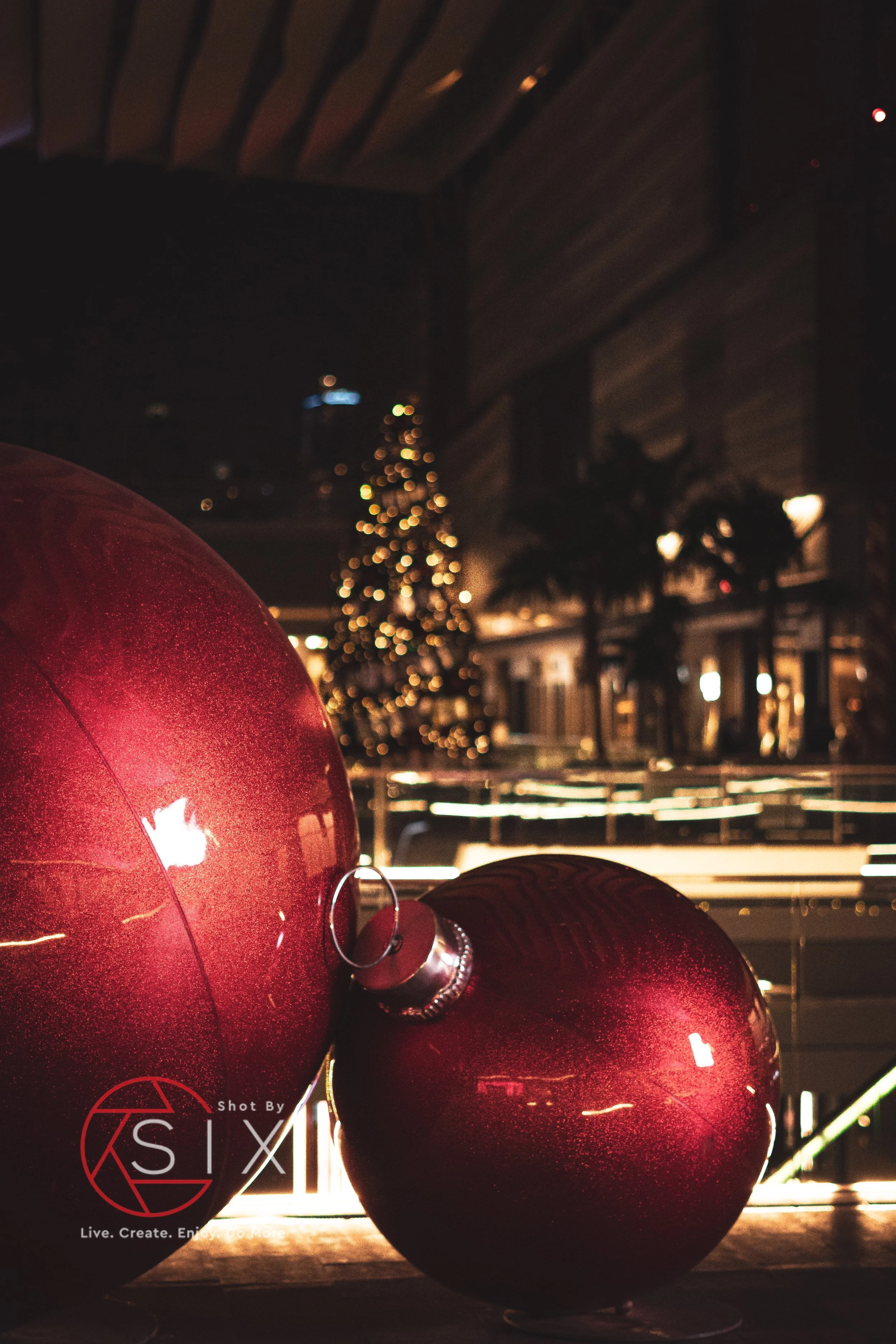 Close-up of two red Christmas ornaments in front of a blurred Christmas tree with lights in the background.