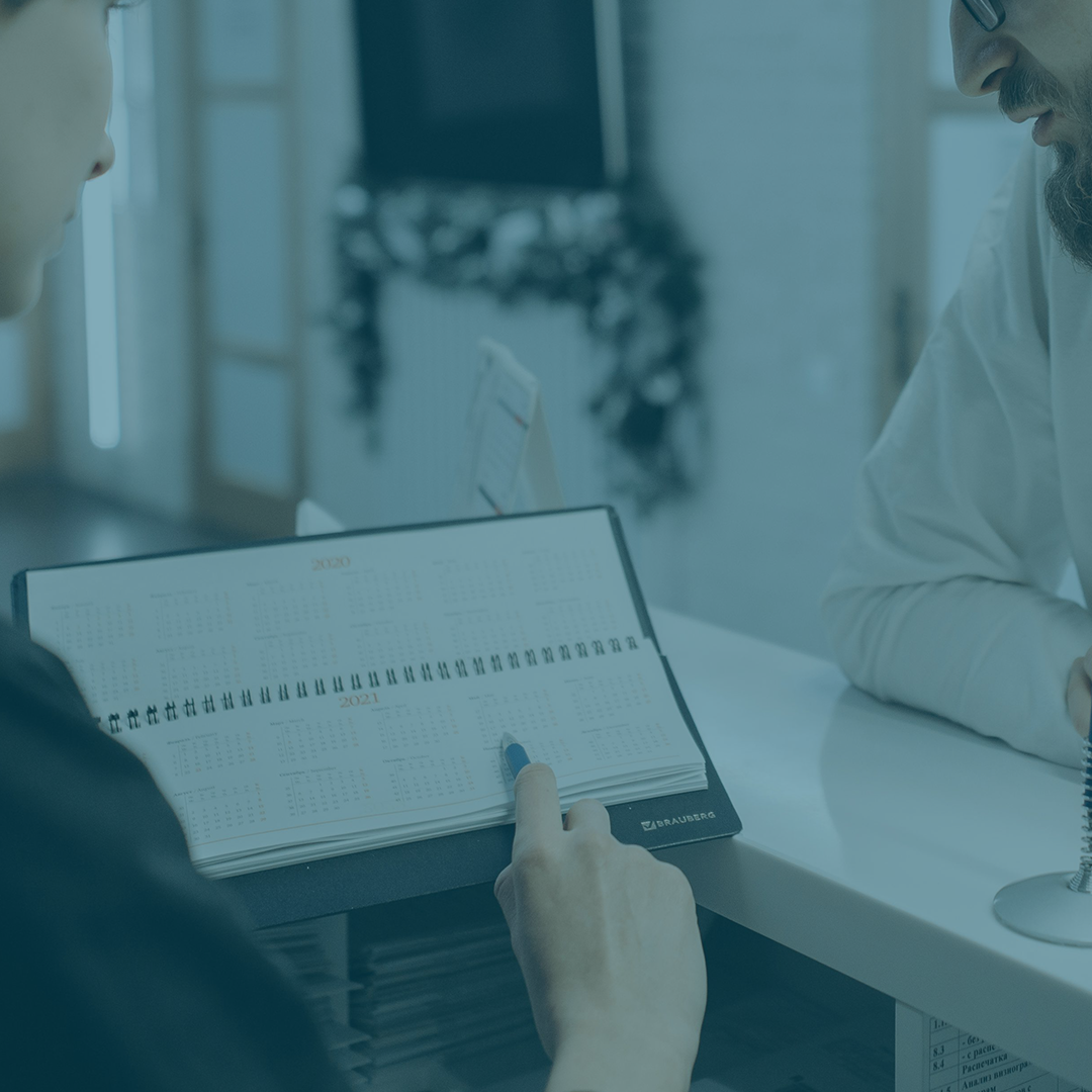 A blue tinted photo of a person making a doctor's appointment with a front desk worker.