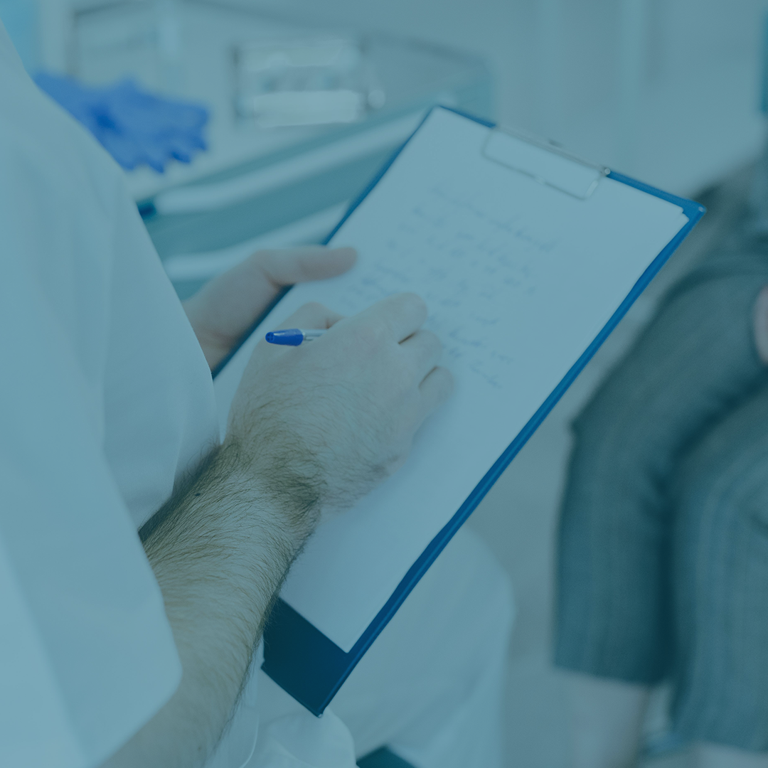 A blue tinted photo of a doctor writing notes for a patient.