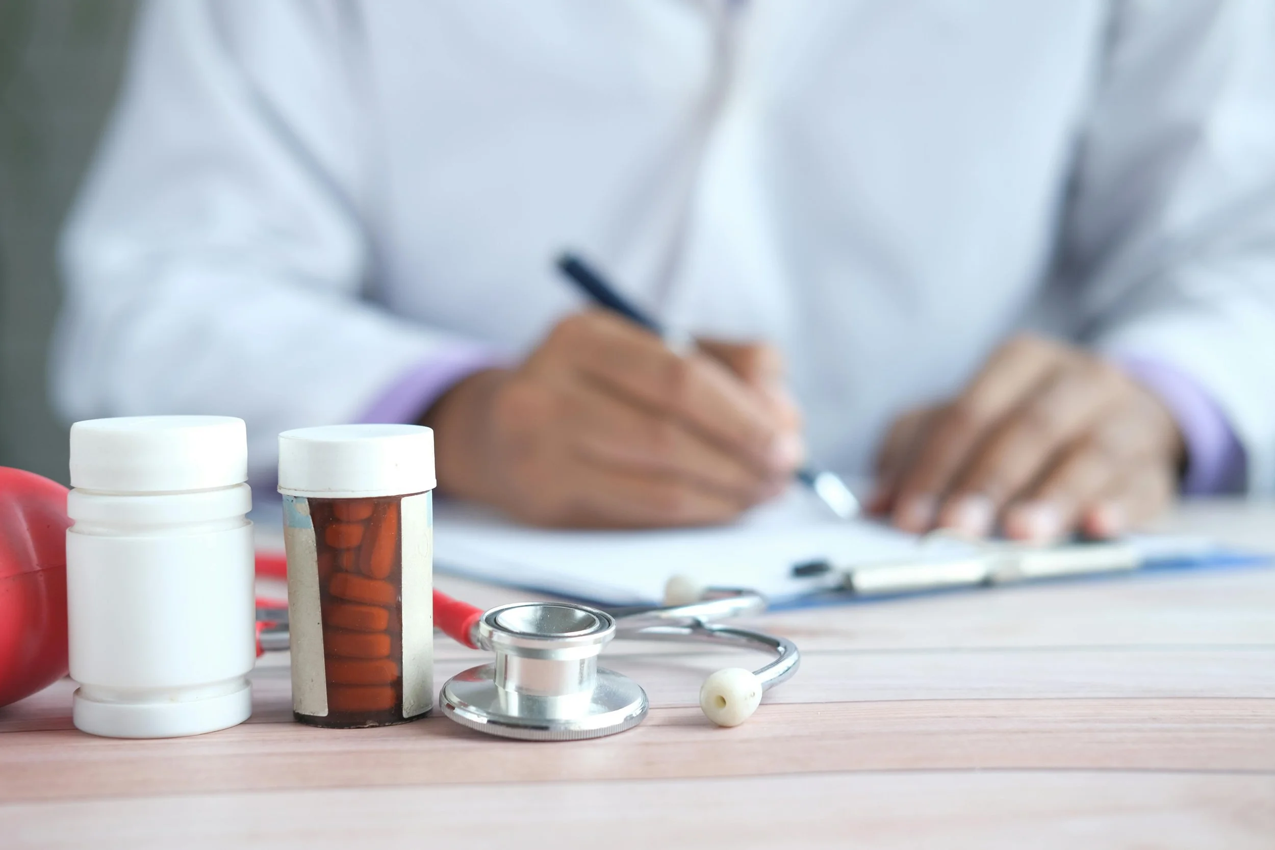 A doctor writing a prescription with medication containers in the foreground.