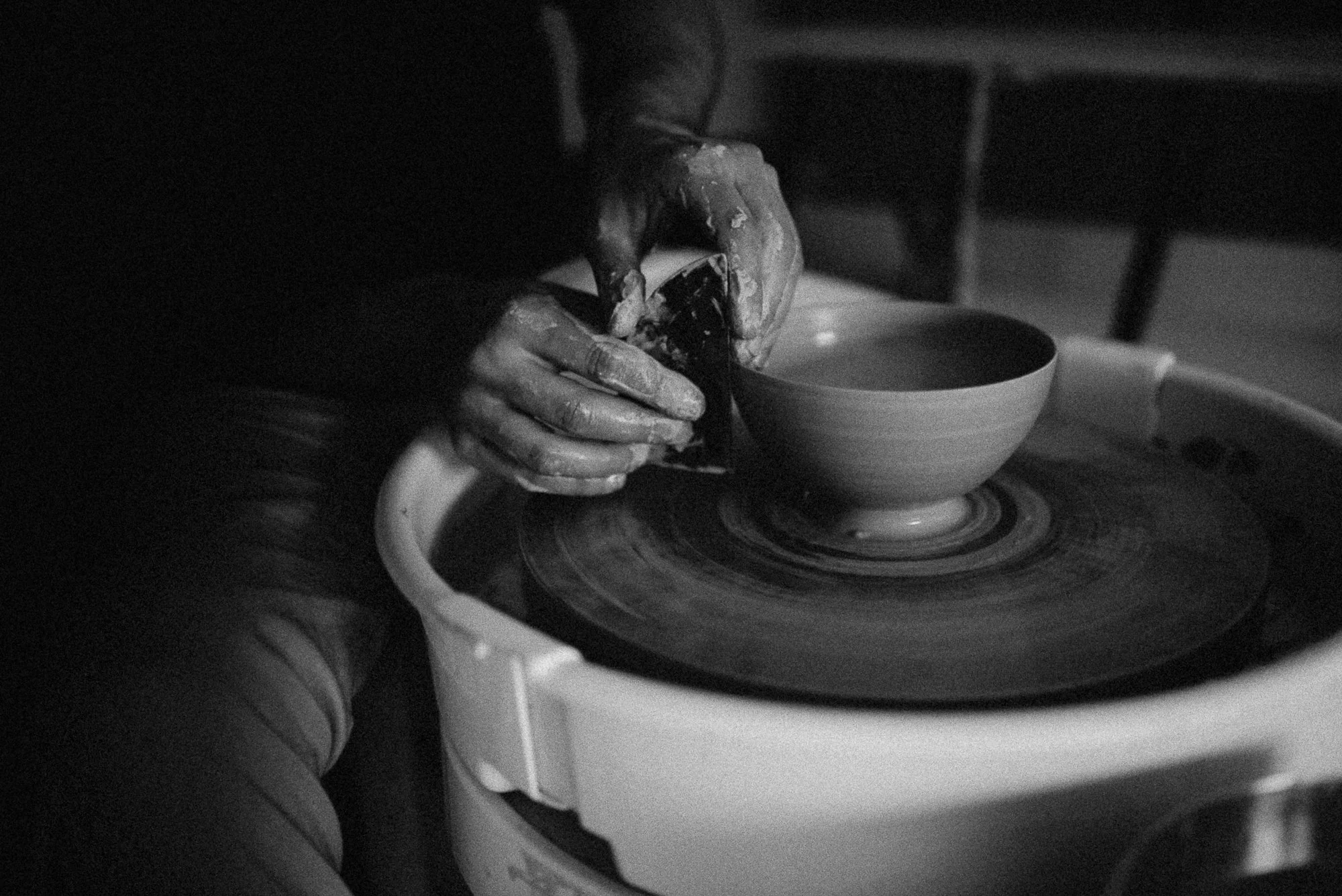 Black and white photo of hands shaping a clay bowl on a pottery wheel.