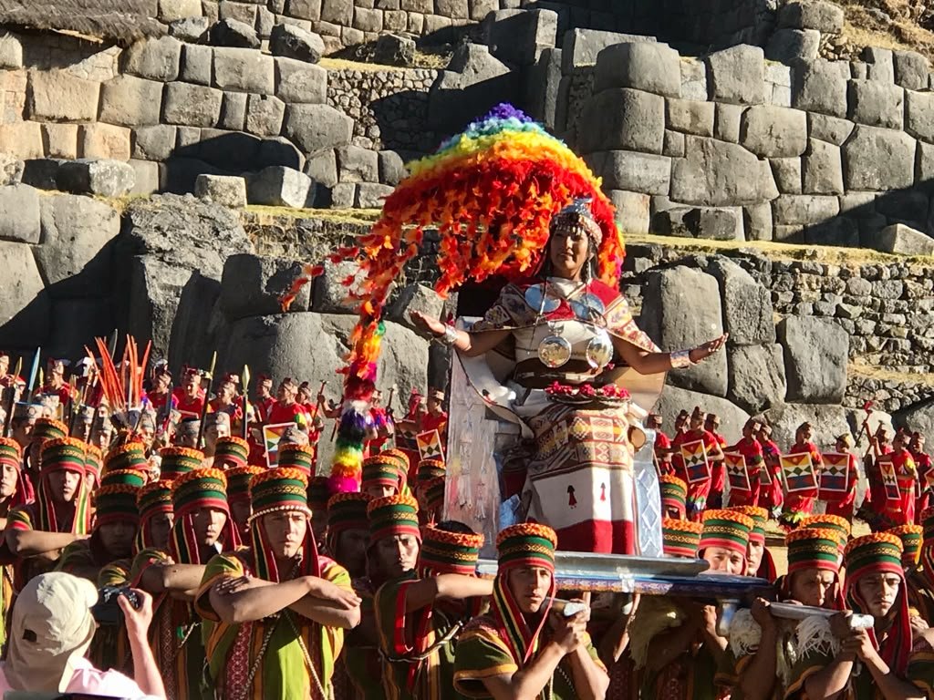 The Inca Queen arrives seated on a silver-plated throne, wearing the silver discs of Mamakilla, borne on a platform carried by dozens of men in ceremonial textile dress.