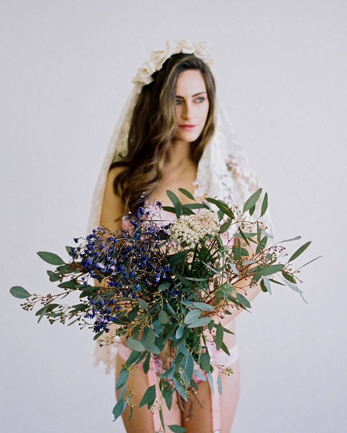 A woman wearing a bridal veil and holding a bouquet of mixed flowers and green foliage.