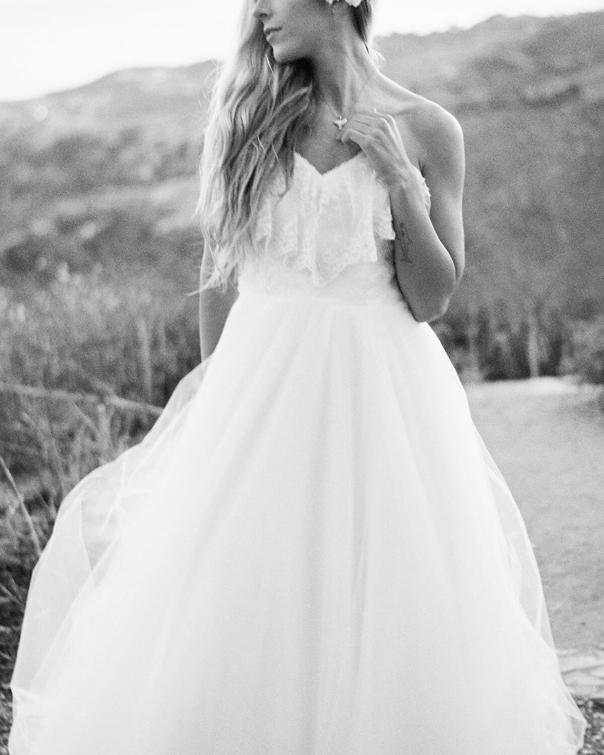 Black-and-white portrait of a bride in a flowing strapless wedding gown outdoors with hills in the background