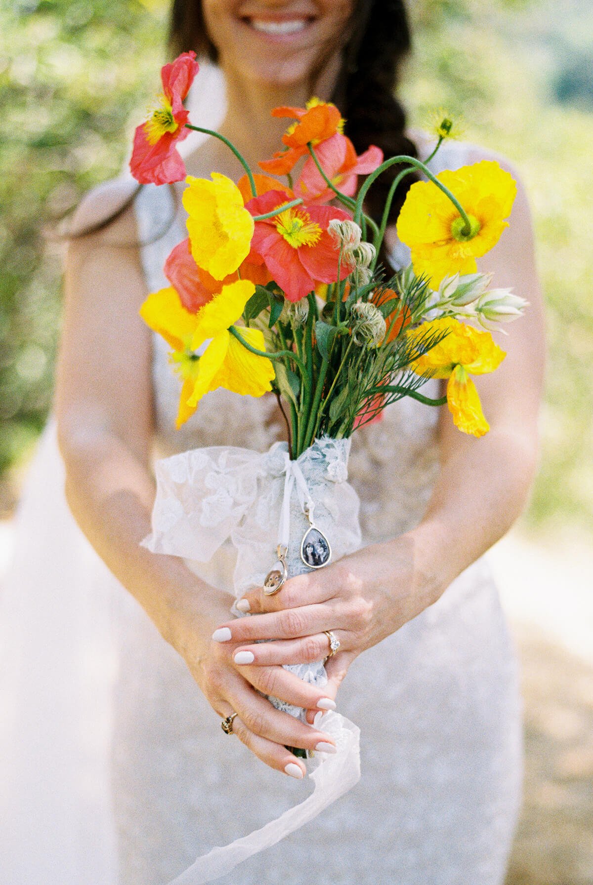 Woman in a wedding dress holding a mixed bouquet of yellow, orange, and pink flowers wrapped in white lace.