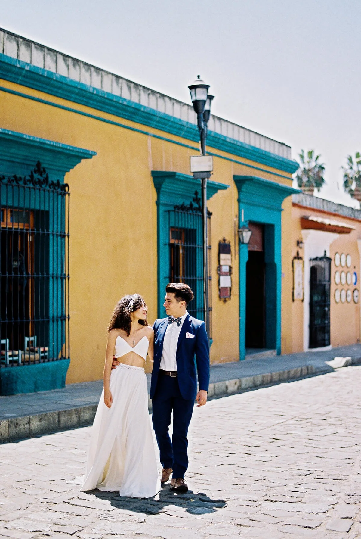 Newlywed couple walking on a cobblestone street in front of a colorful colonial building