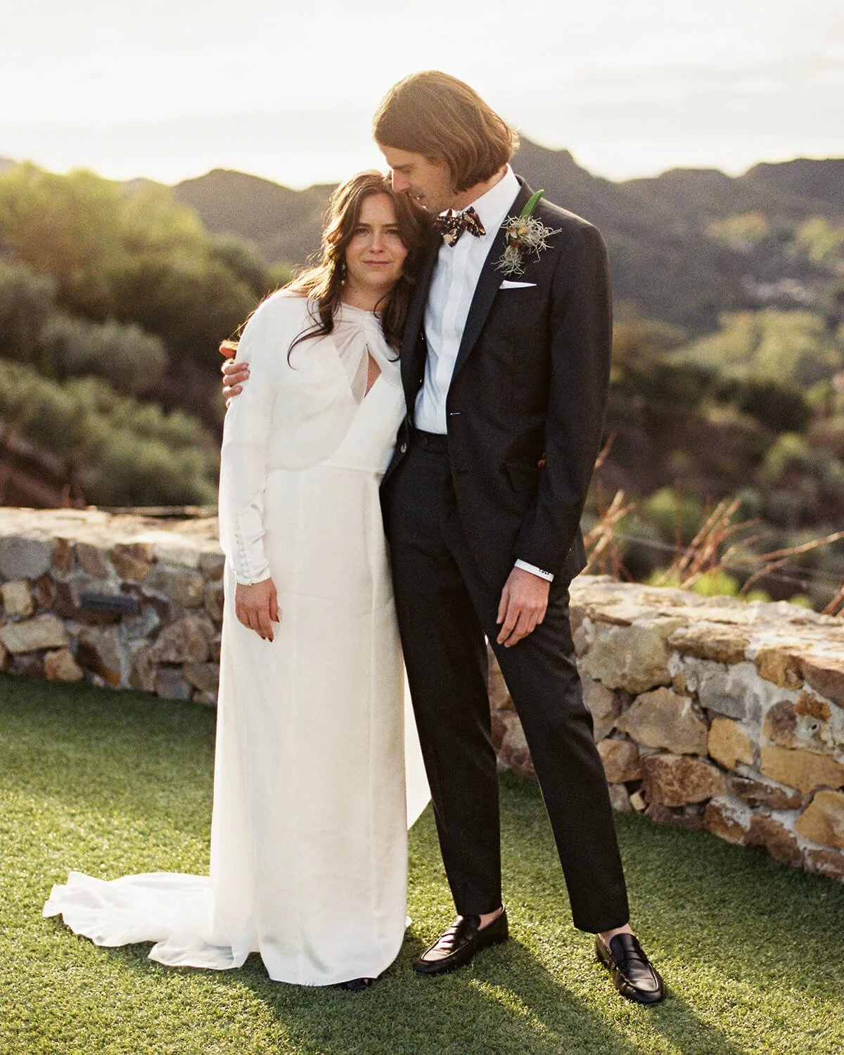 A bride and groom standing together outdoors on their wedding day, with a rocky landscape and mountains in the background at Cielo Farms in Malibu.