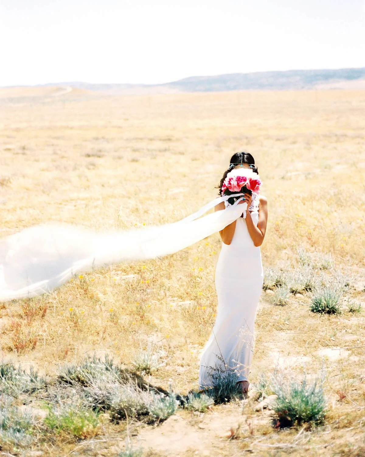 A Quinceañera in a white dress holding a pink bouquet in a desert landscape.