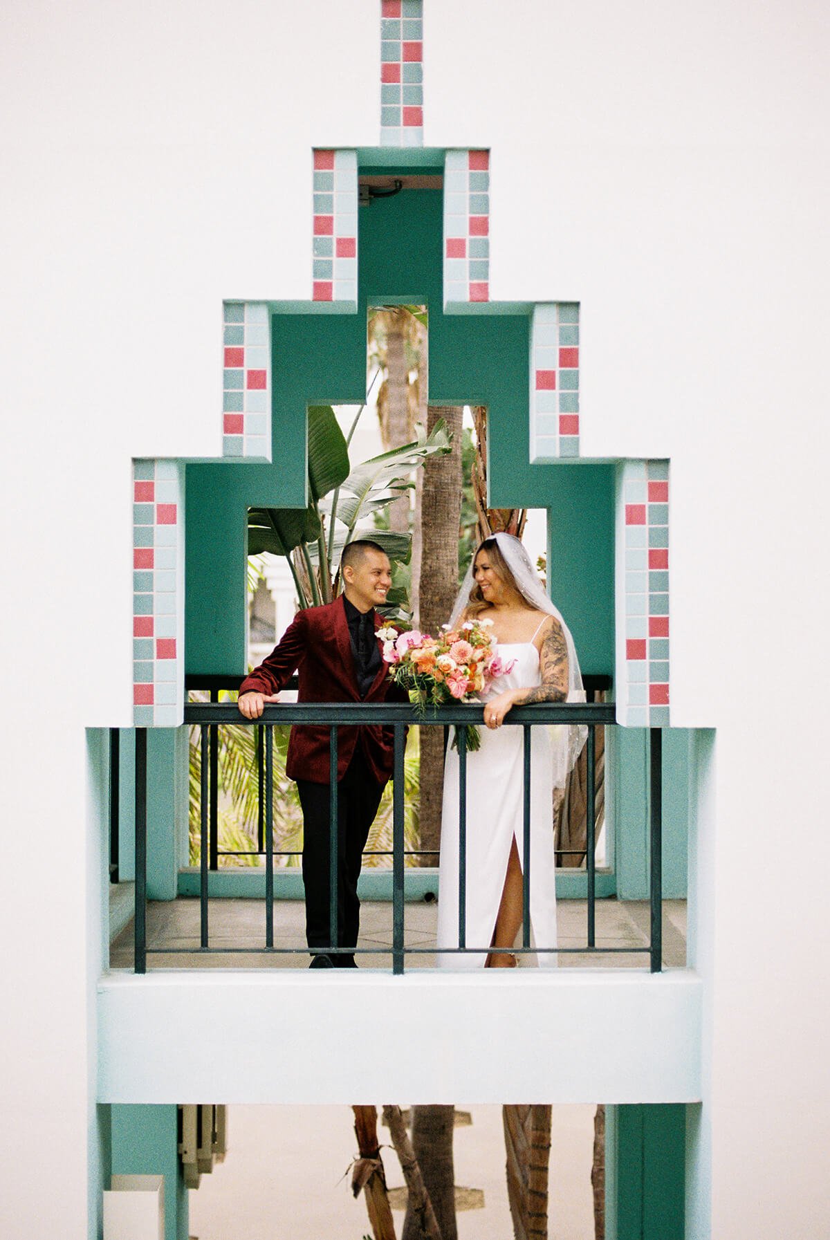 Bride and groom standing on a balcony framed by a decorative architectural opening with Star Wars theme, holding a bouquet, smiling at each other.