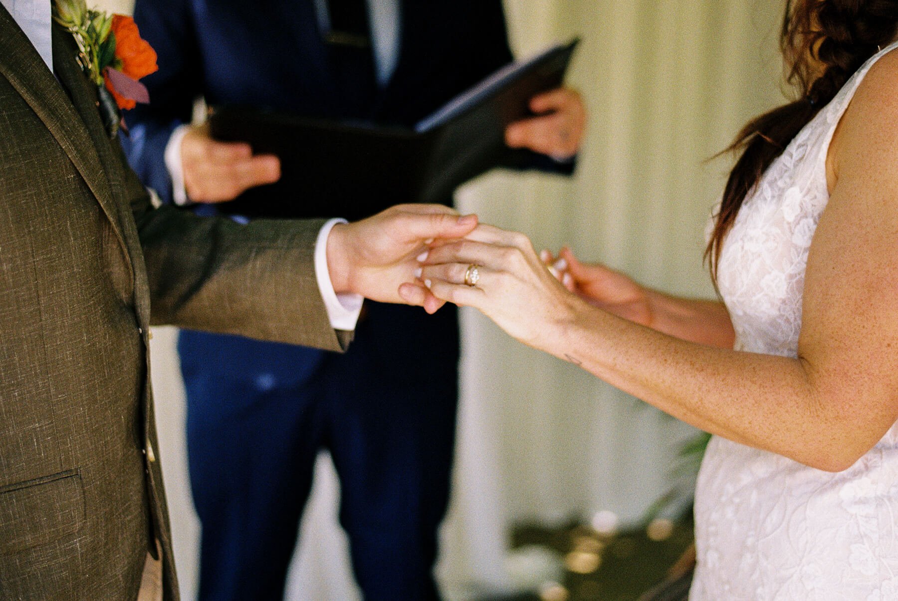 A bride and groom holding hands during their wedding ceremony, with an officiant in the background.
