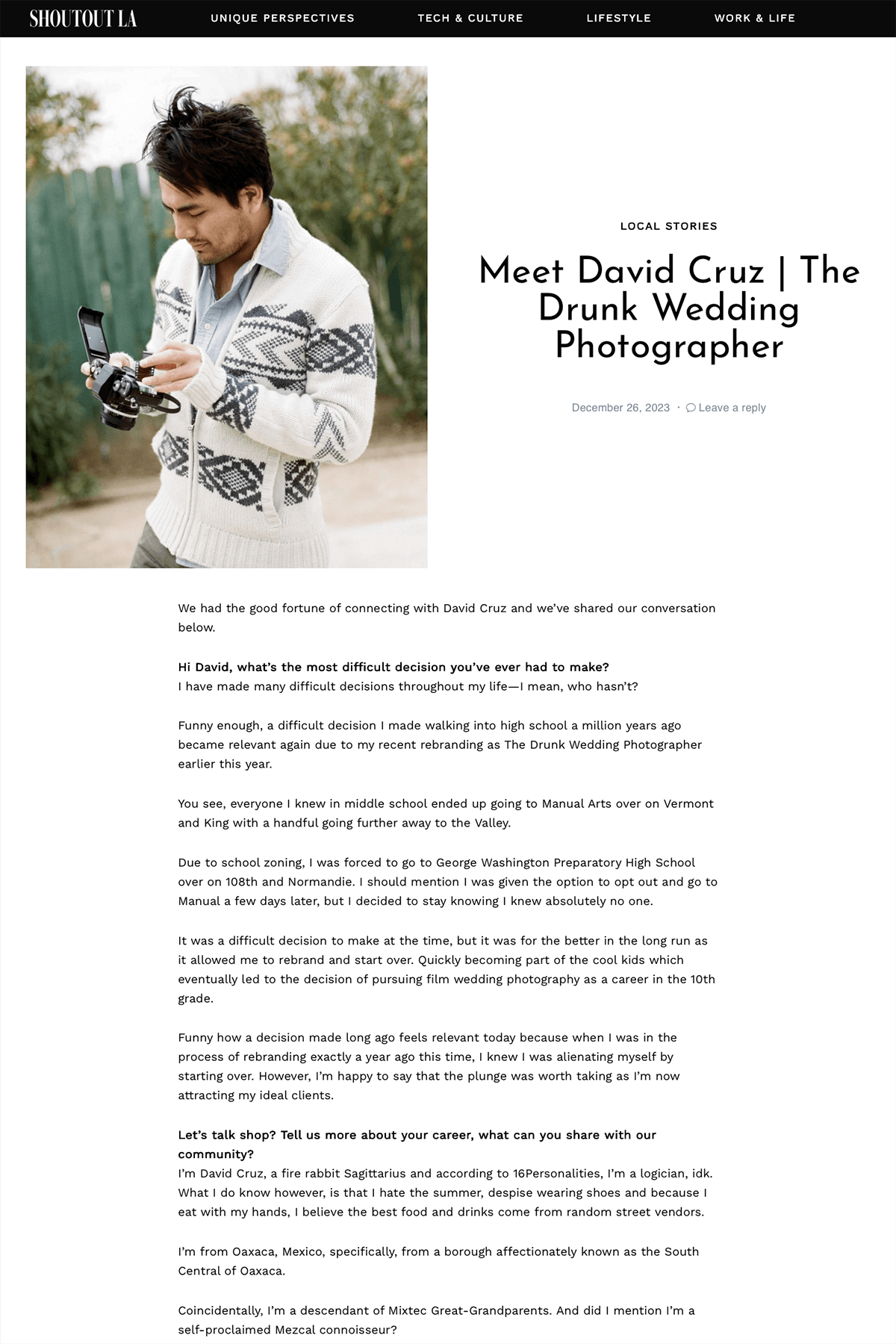 David Cruz The Drunk Wedding Photographer with dark hair wearing a white sweater with blue geometric patterns, looking at a camera in an outdoor setting with trees and a green fence in the background.