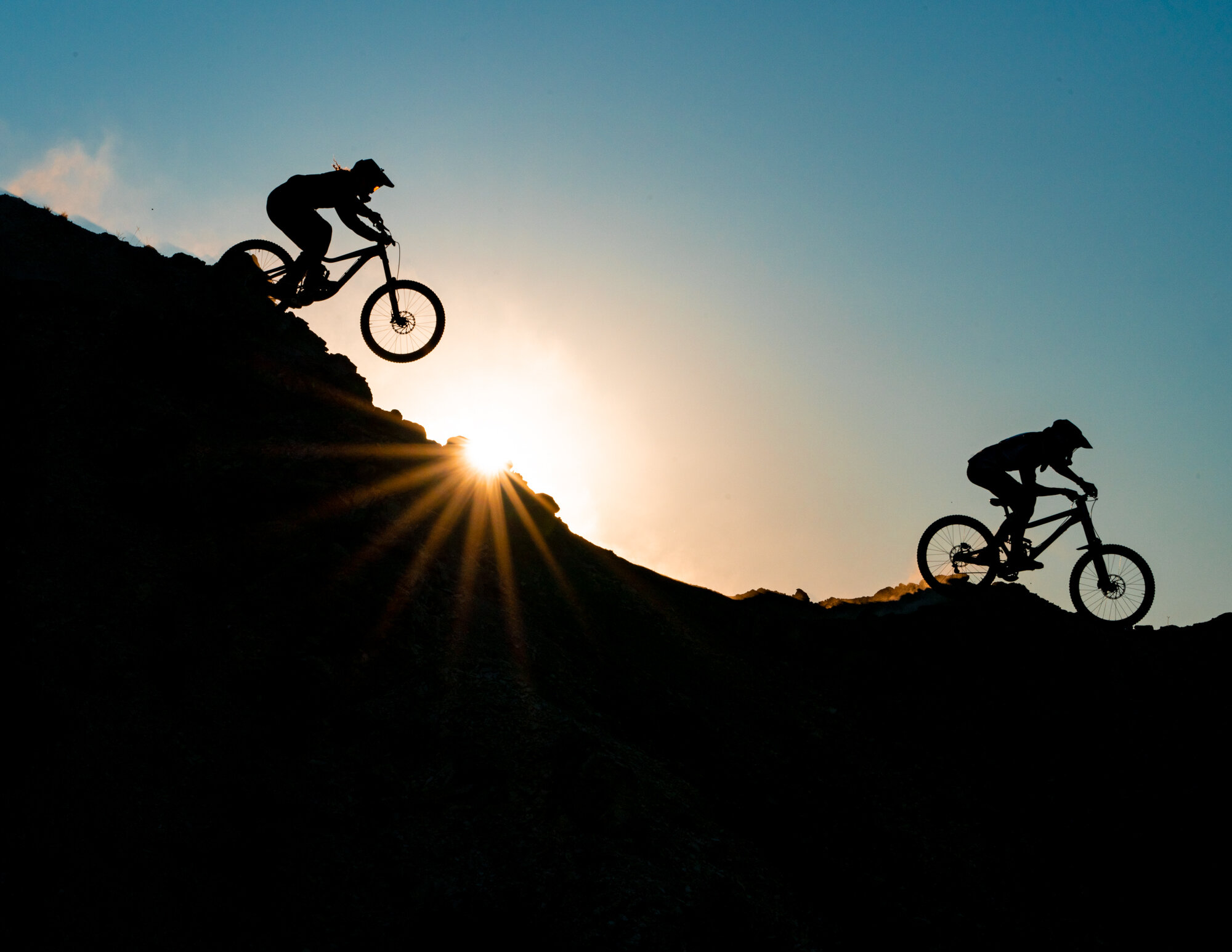 Action sports photography hero shot of two silhouetted mountain bikers speeding down a ridge as the sun rises.

Riders are Sage Cattabriga-Alosa and Henry Lanman