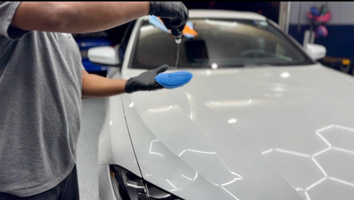applying a cleaning  to the hood of a silver car in a garage.