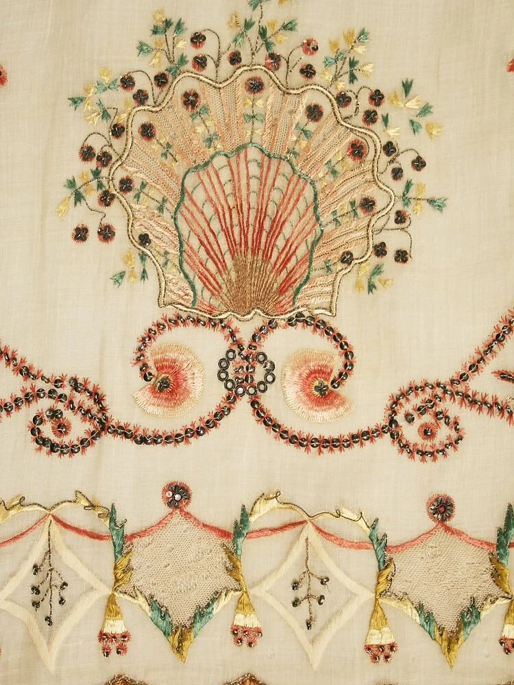 Yesterday&rsquo;s gown was embroidered with scallop shells. Today&rsquo;s, dating from around 1810 and thought to have been made in Spain, carries them too &mdash; large scallops stitched around the hem of an ethereal pi&ntilde;a muslin overdress.

P