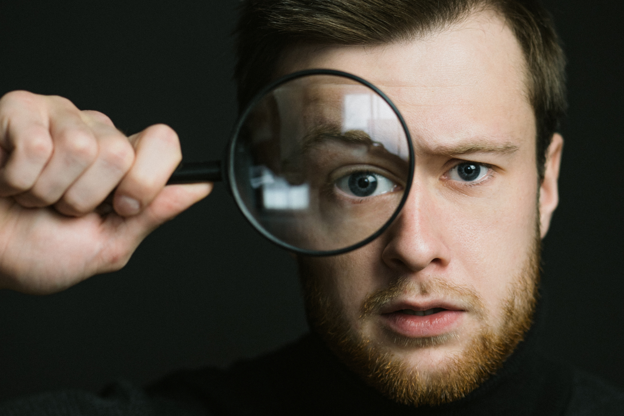 Man examining one eye through a magnifying glass, illustrating diagnosing the real cause of team stress before booking training