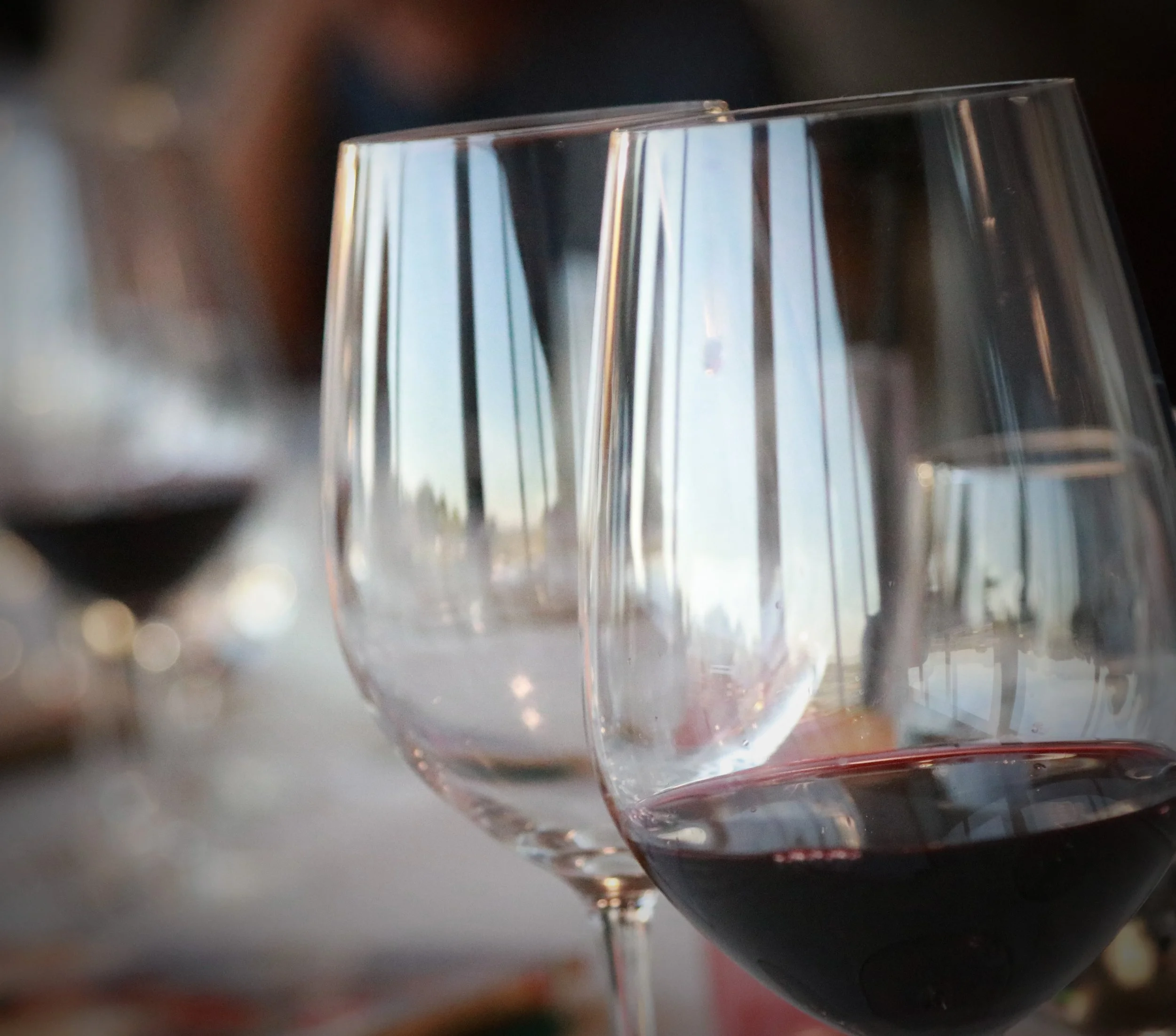 Close-up of two wine glasses, one with red wine and one empty, on a table at a social gathering.
