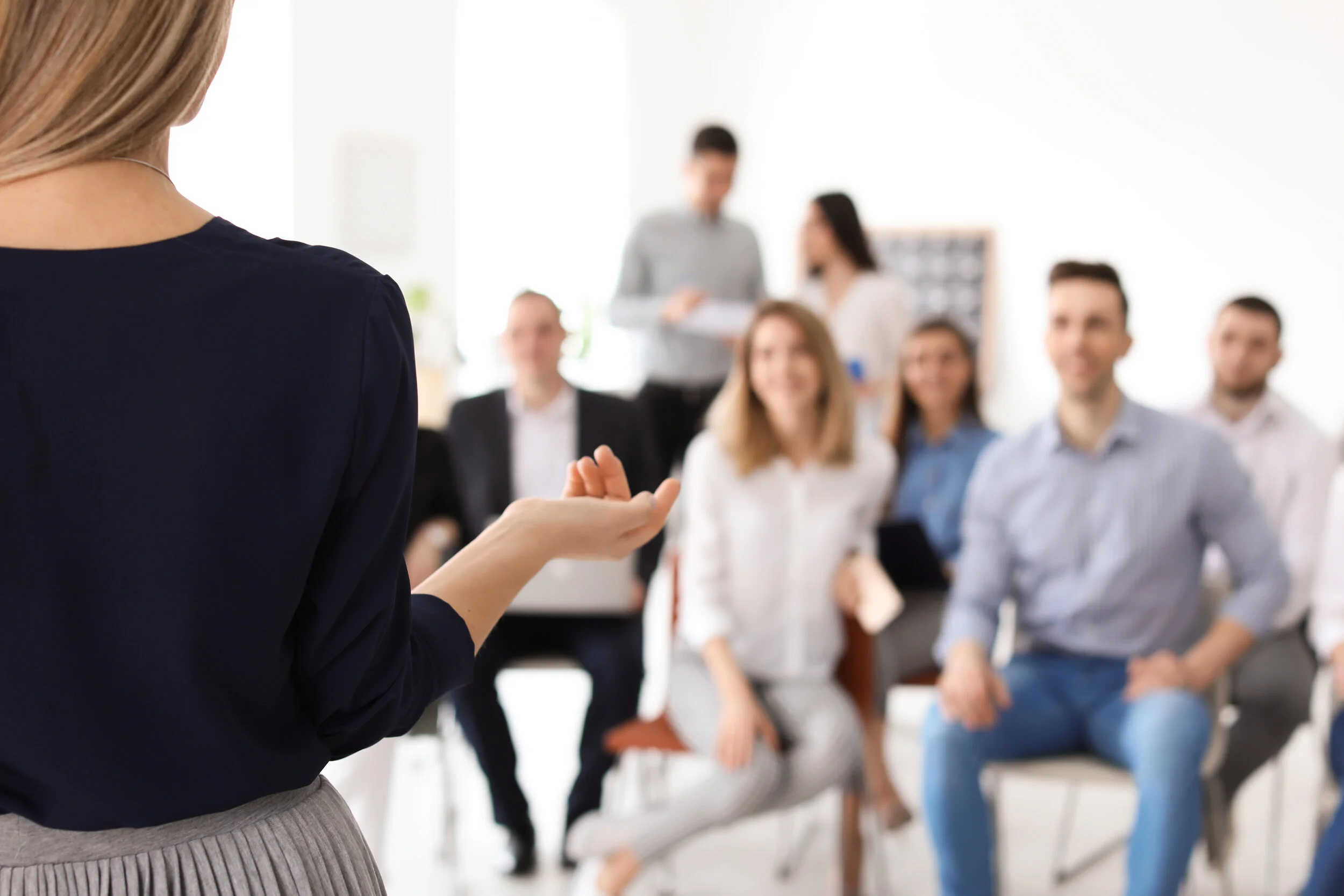 Woman giving a presentation to a room with adults sitting down watching her