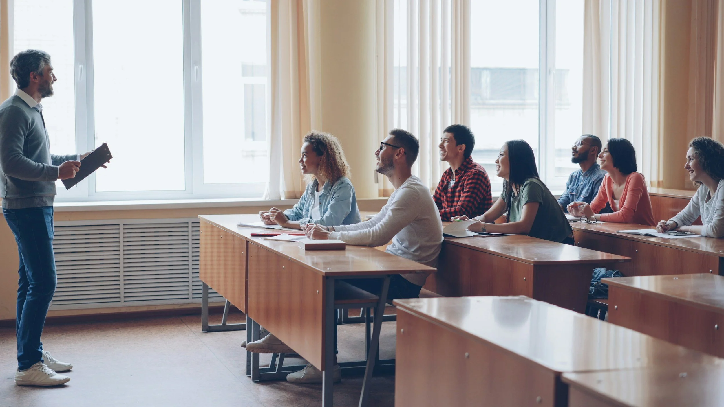 Diverse group of young students sitting at desks in a bright well-lit room