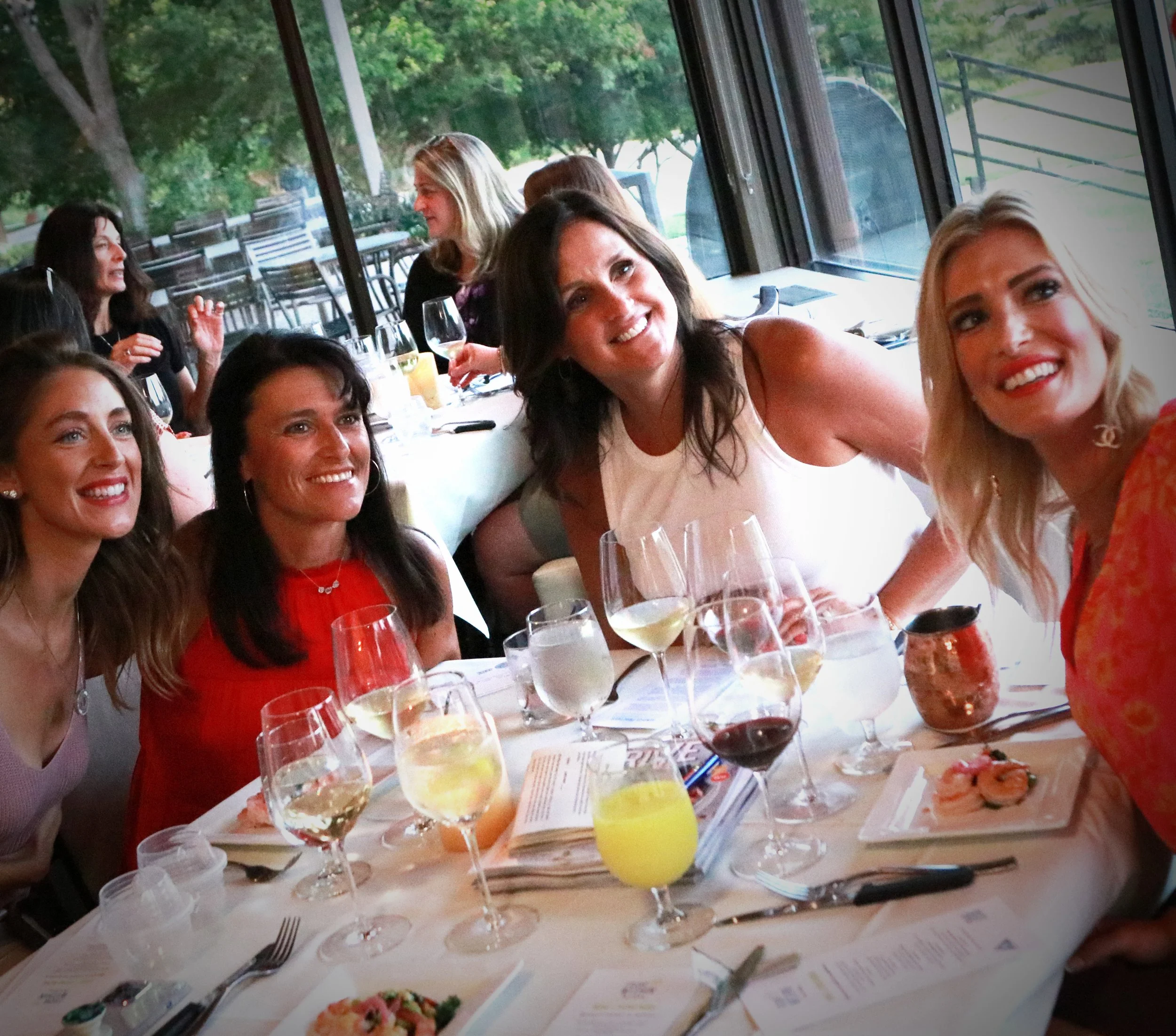 A group of women enjoying a meal at a restaurant, smiling and posing for a photo with a table full of drinks and plates of food.