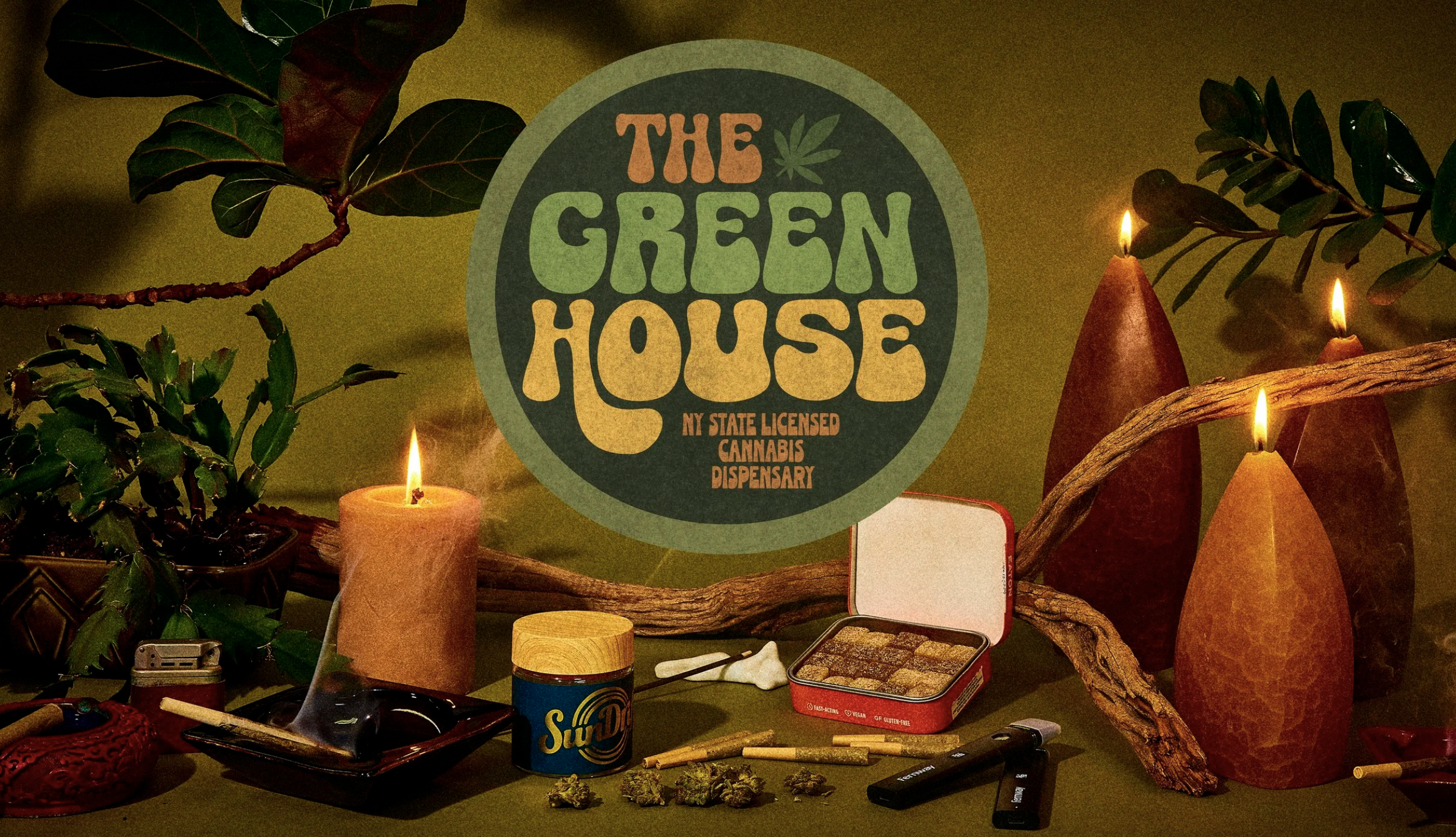 Display of cannabis products and smoking accessories with a sign reading 'The Green House NY State Licensed Cannabis Dispensary', surrounded by candles and decorative elements.