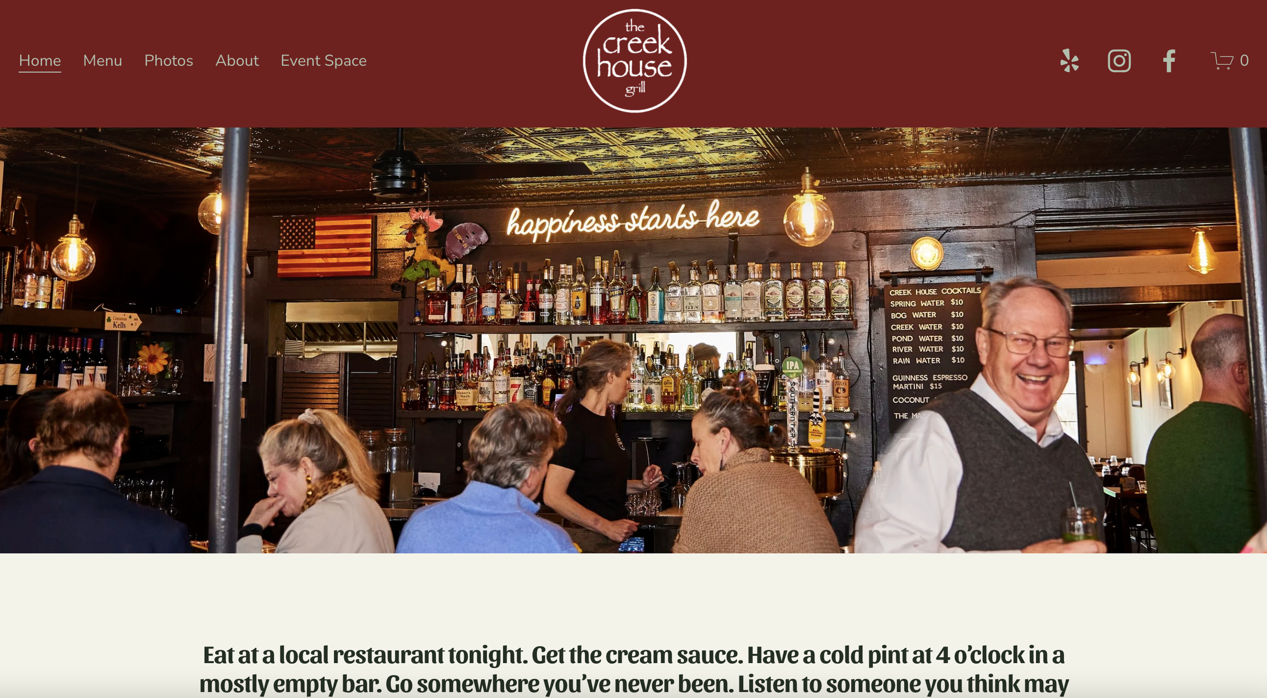 Interior view of The Creek House Grill bar with customers seated and socializing, shelves stocked with bottles of alcohol, a neon sign reading "happiness starts here", and a menu on the wall listing various drinks.