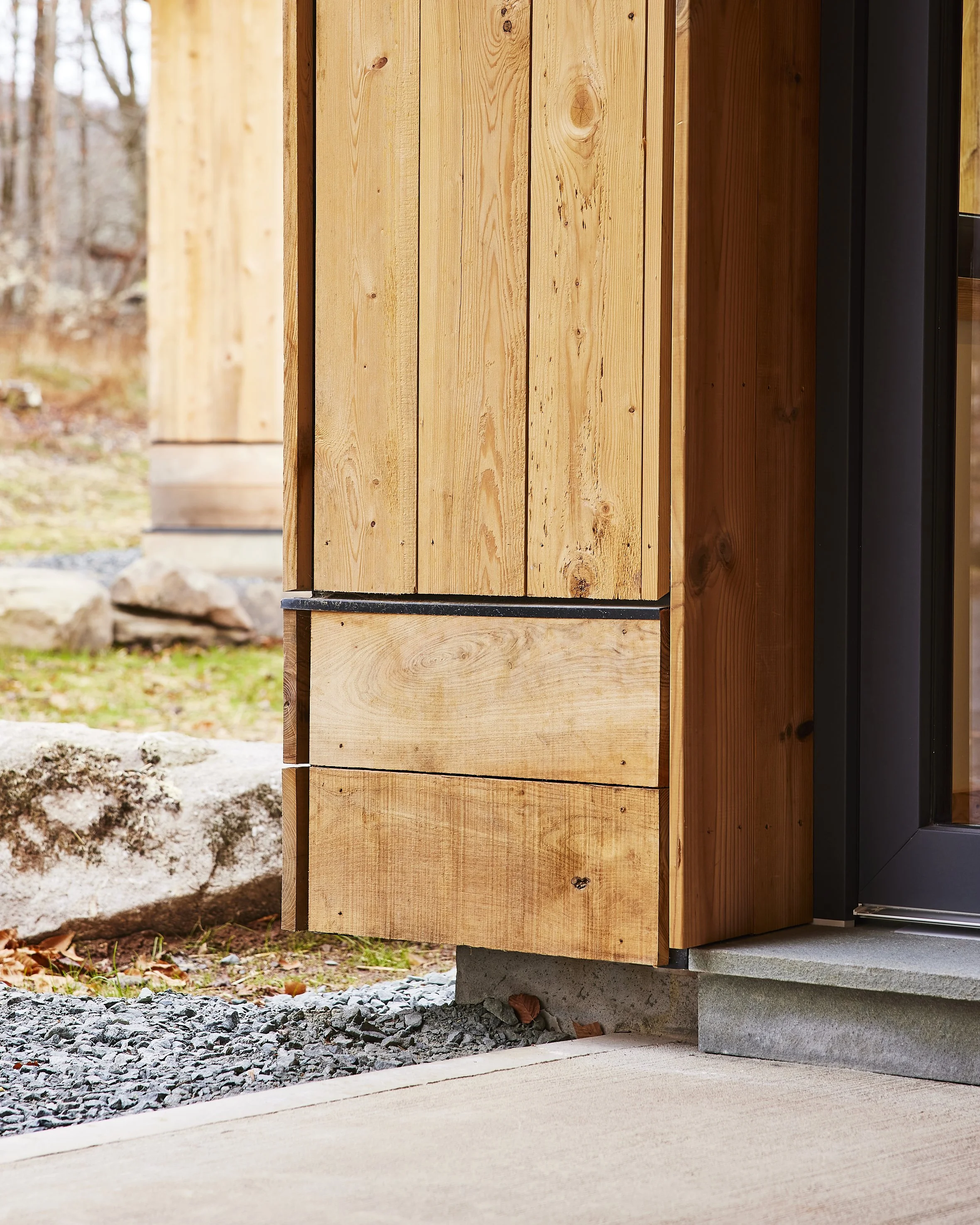 Close-up of a house corner with wooden siding, concrete steps, and a glass door.
