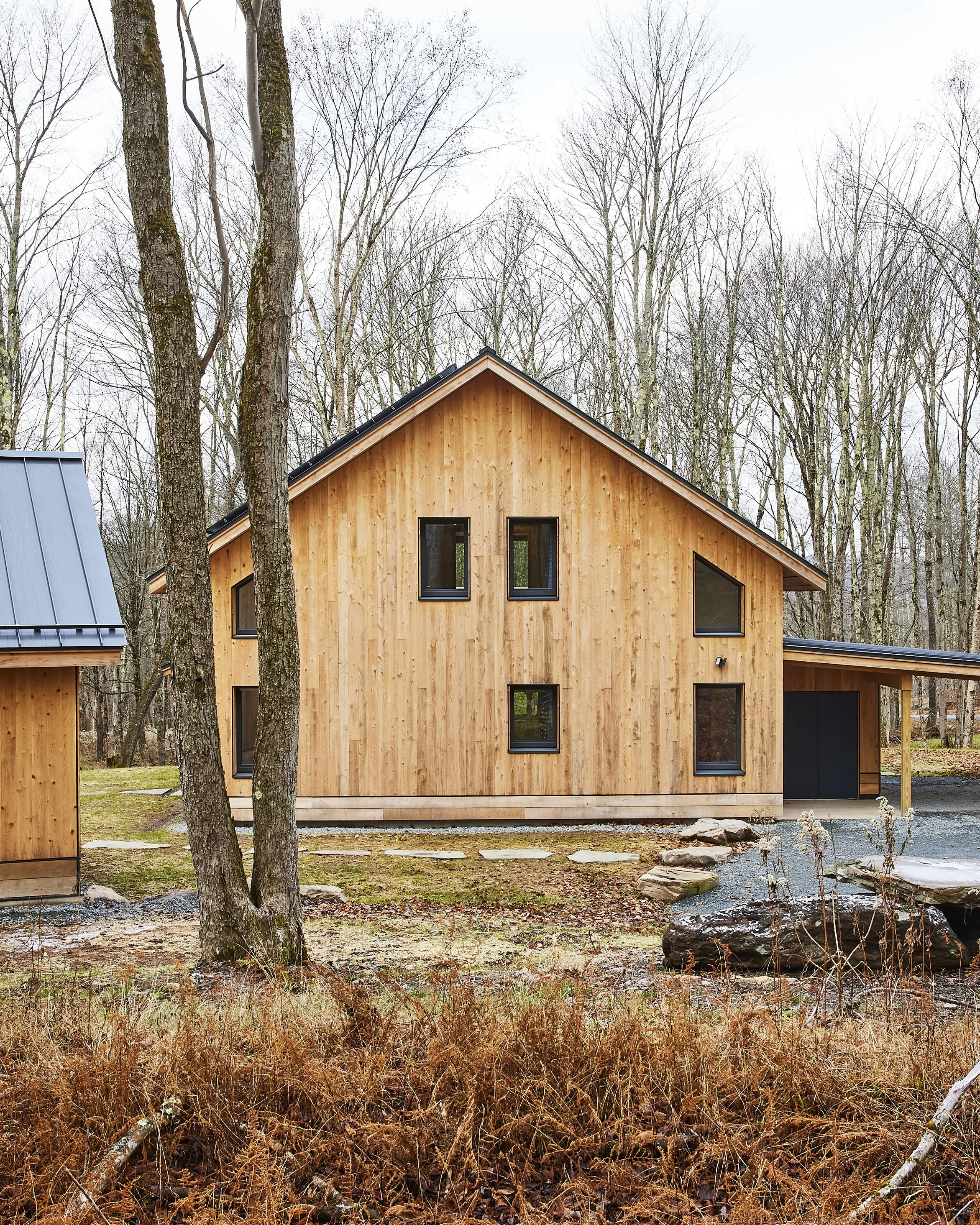 Modern wooden house with black-framed windows surrounded by trees and natural landscape.