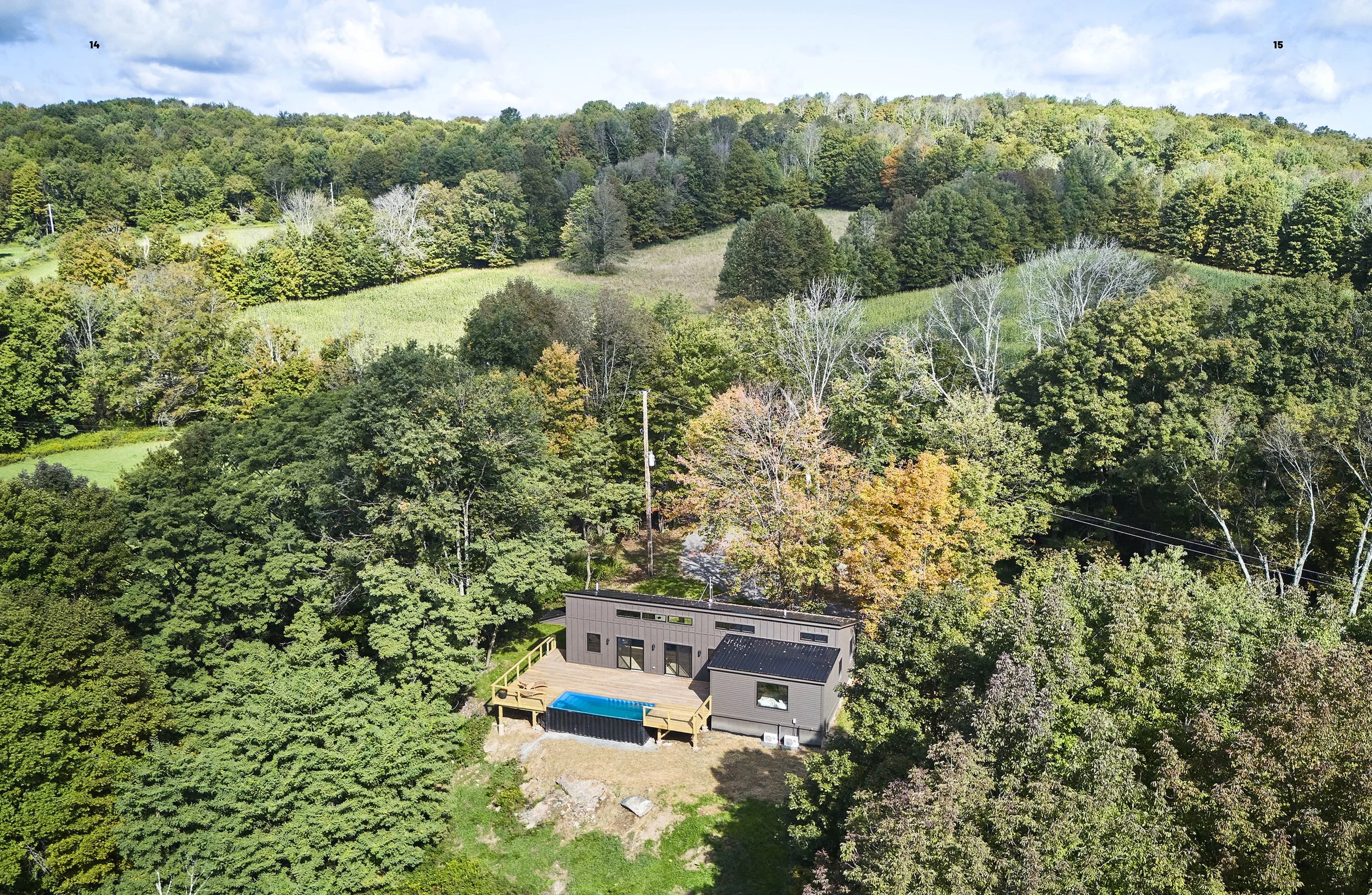A modern house with a deck and a small pool, surrounded by trees and hills in the background.
