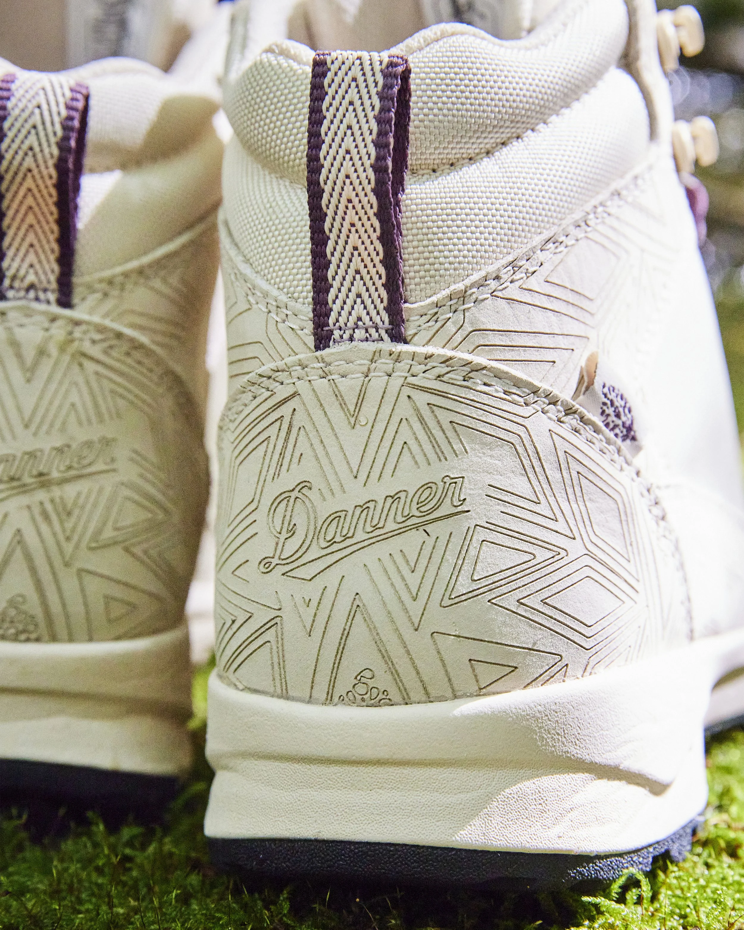 Close-up of a white athletic shoe with the brand name 'Danner' embossed on the heel, showing intricate geometric line patterns.