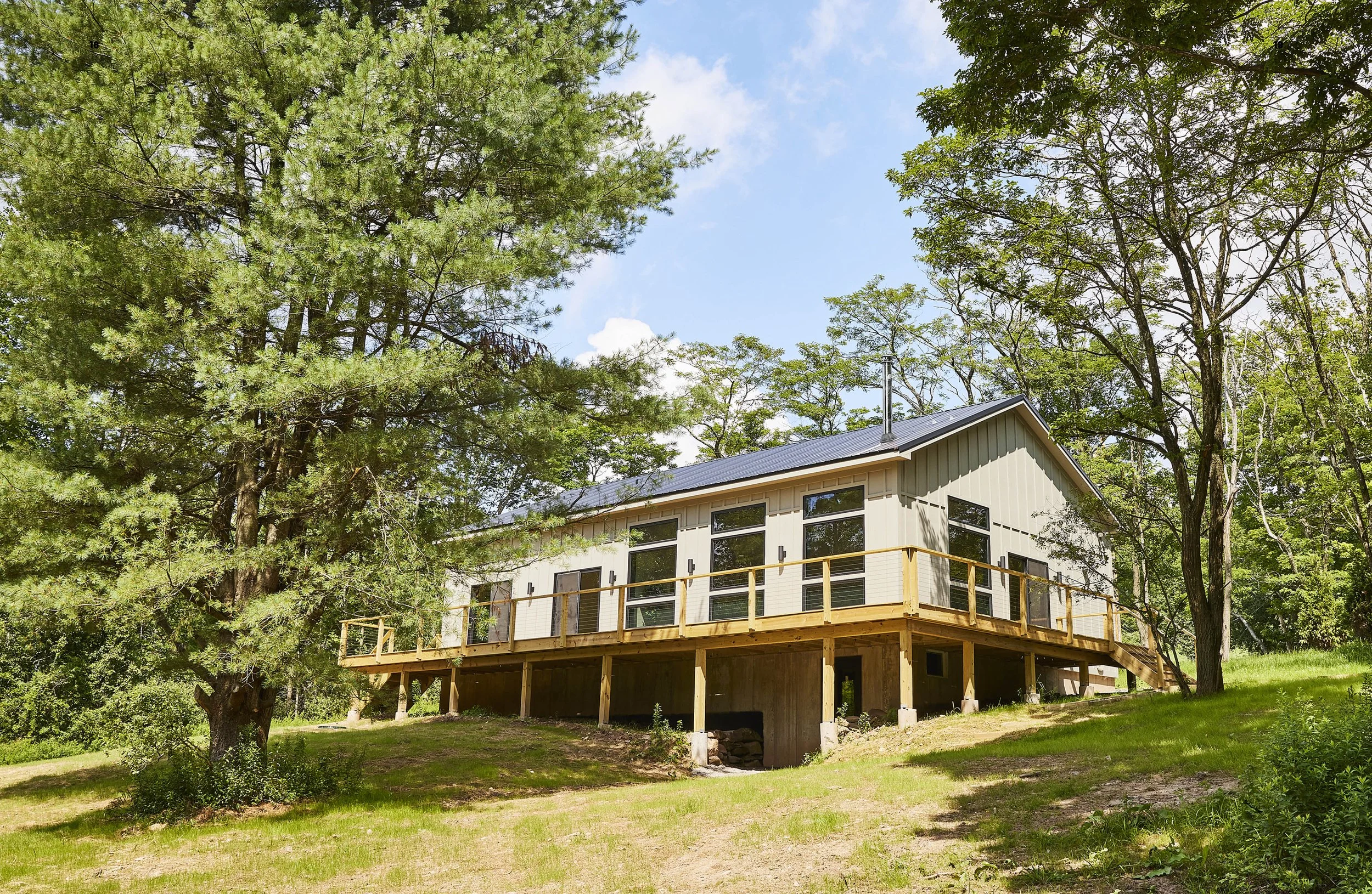 Modern house under construction on a grassy hill with trees and blue sky in the background