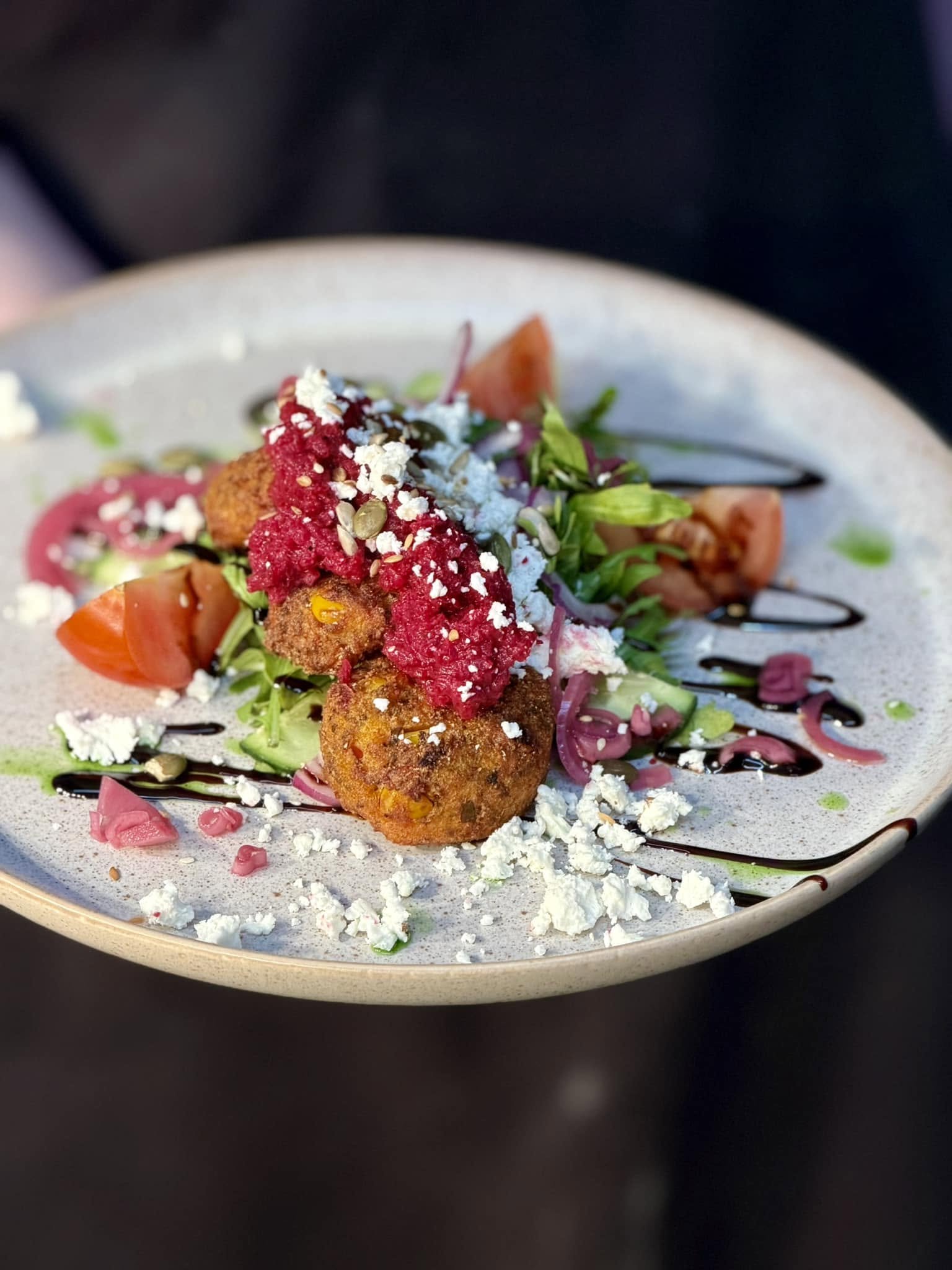 A plate of salad with falafel, chopped vegetables, crumbled cheese, and a drizzle of balsamic glaze.