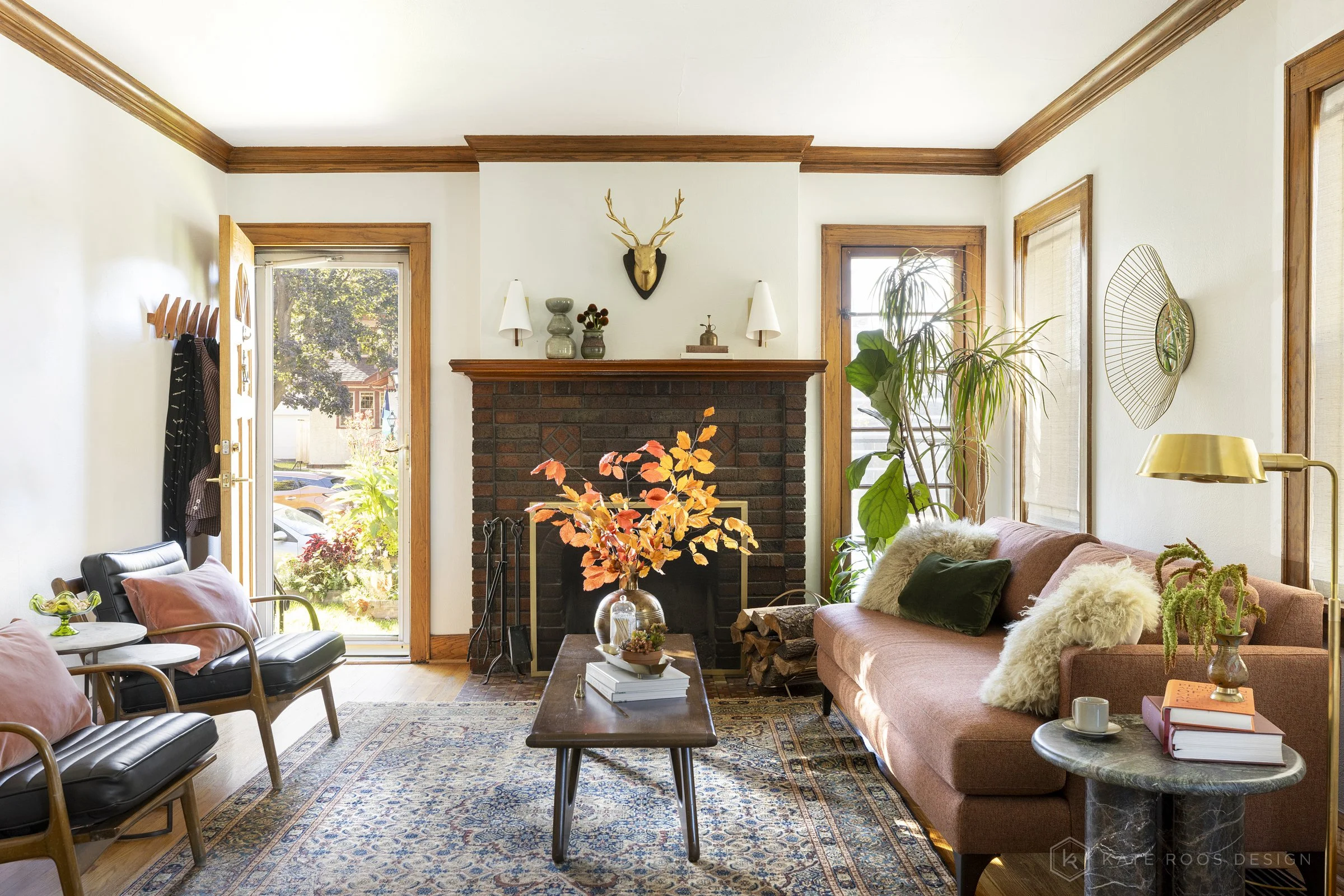 This curated living and dining room showcases a warm modern traditional interior design with strong mid-century modern influences. Original hardwood floors, rich stained wood trim, and a classic arched doorway highlight the home’s historic character 