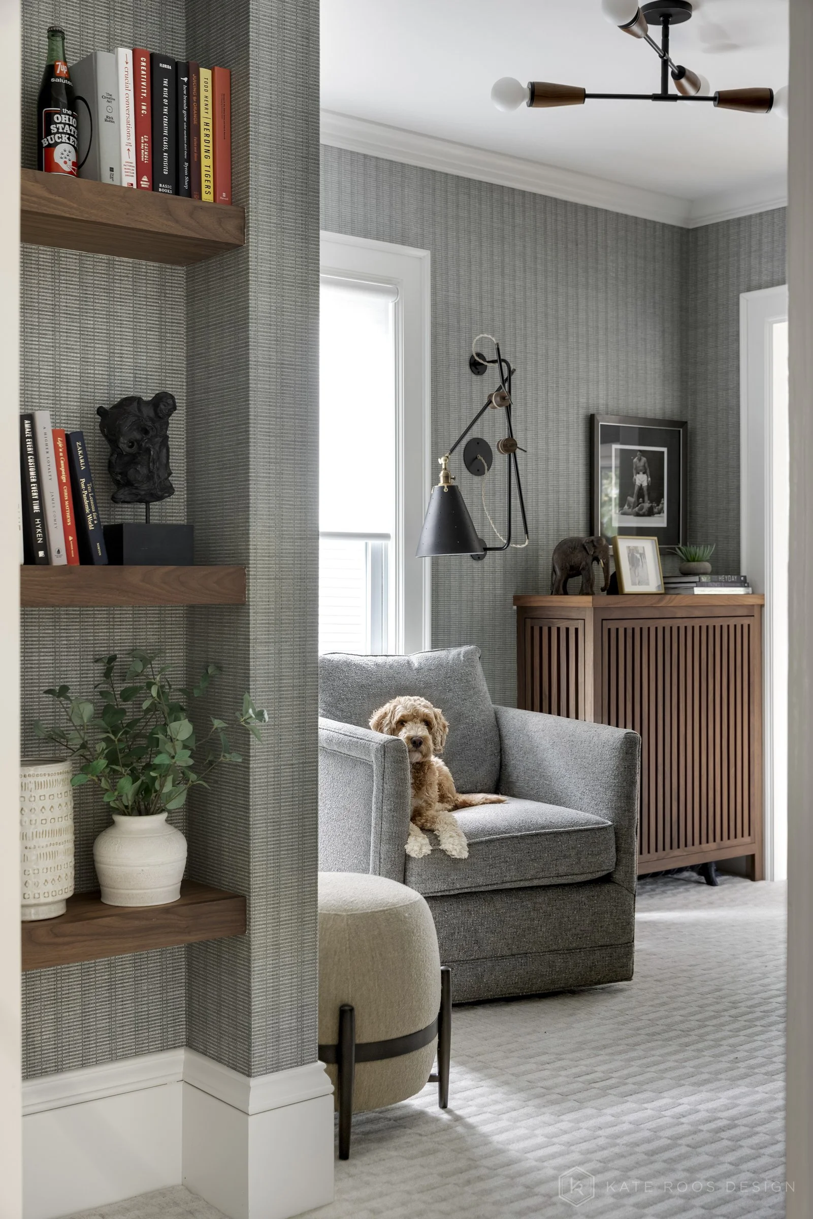 This image showcases a beautifully designed home office that balances function, comfort, and style. The space features a built-in desk with rich wood countertops and deep navy cabinetry accented by brass hardware, creating a sophisticated yet invitin