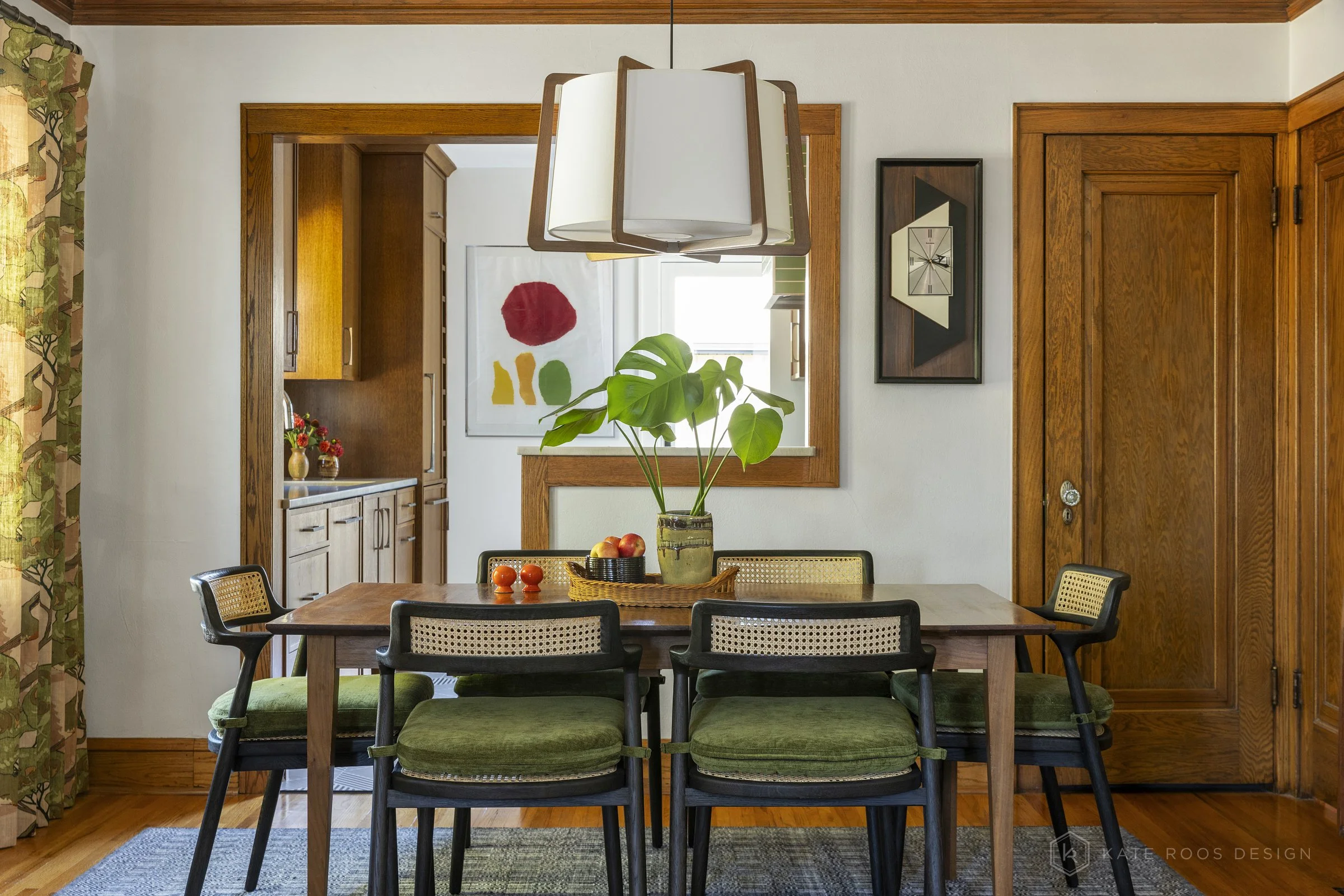 This curated living and dining room showcases a warm modern traditional interior design with strong mid-century modern influences. Original hardwood floors, rich stained wood trim, and a classic arched doorway highlight the home’s historic character 