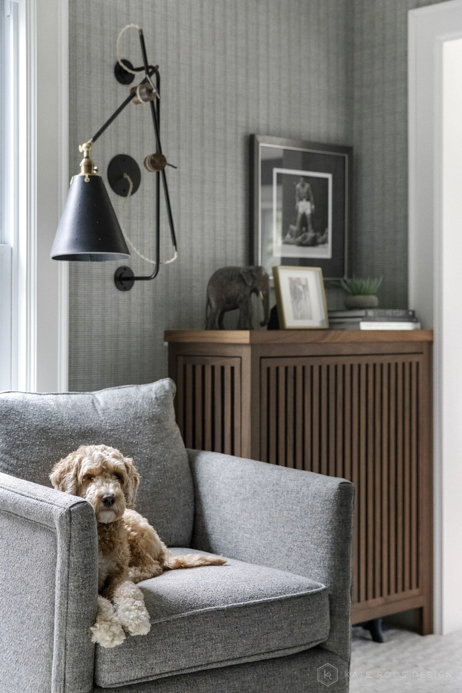 This image showcases a beautifully designed home office that balances function, comfort, and style. The space features a built-in desk with rich wood countertops and deep navy cabinetry accented by brass hardware, creating a sophisticated yet invitin
