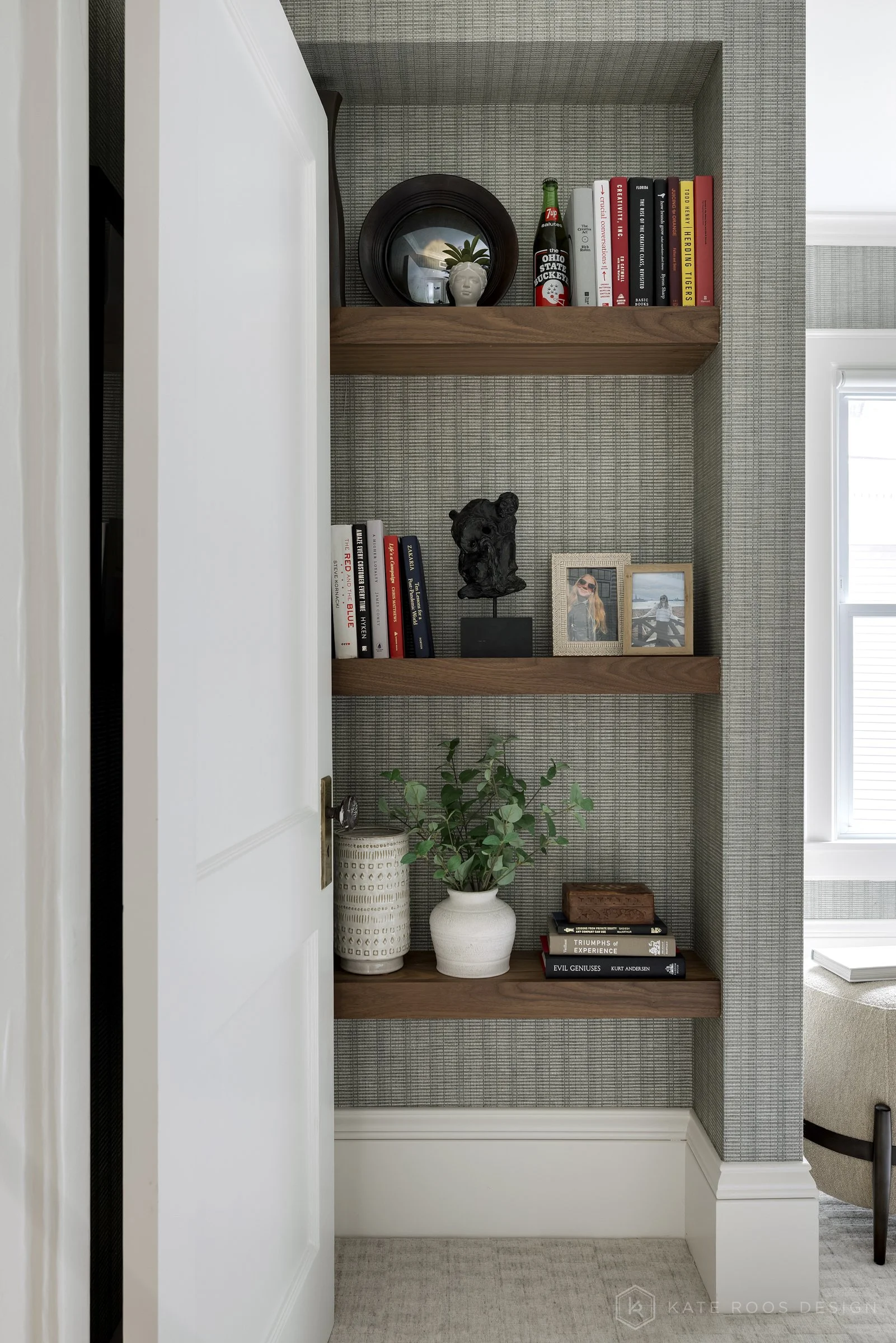 This image showcases a beautifully designed home office that balances function, comfort, and style. The space features a built-in desk with rich wood countertops and deep navy cabinetry accented by brass hardware, creating a sophisticated yet invitin