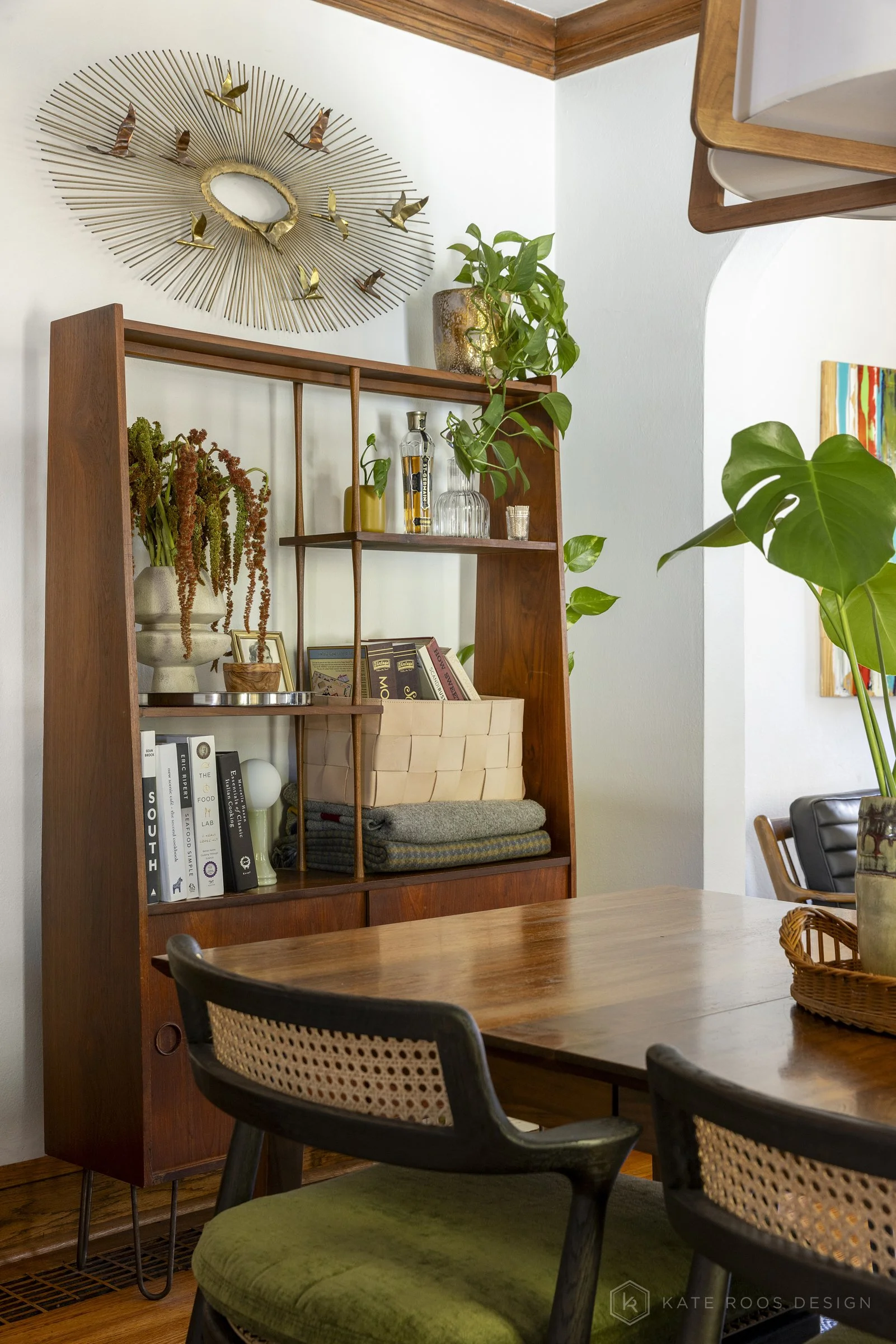 This curated living and dining room showcases a warm modern traditional interior design with strong mid-century modern influences. Original hardwood floors, rich stained wood trim, and a classic arched doorway highlight the home’s historic character 