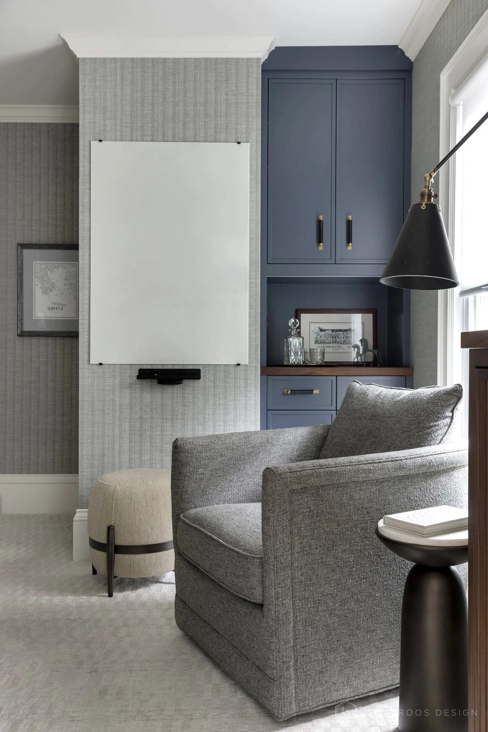 This image showcases a beautifully designed home office that balances function, comfort, and style. The space features a built-in desk with rich wood countertops and deep navy cabinetry accented by brass hardware, creating a sophisticated yet invitin