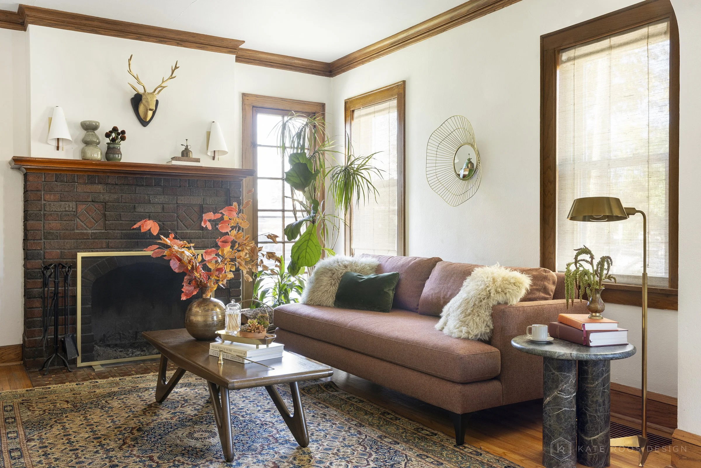 This curated living and dining room showcases a warm modern traditional interior design with strong mid-century modern influences. Original hardwood floors, rich stained wood trim, and a classic arched doorway highlight the home’s historic character 
