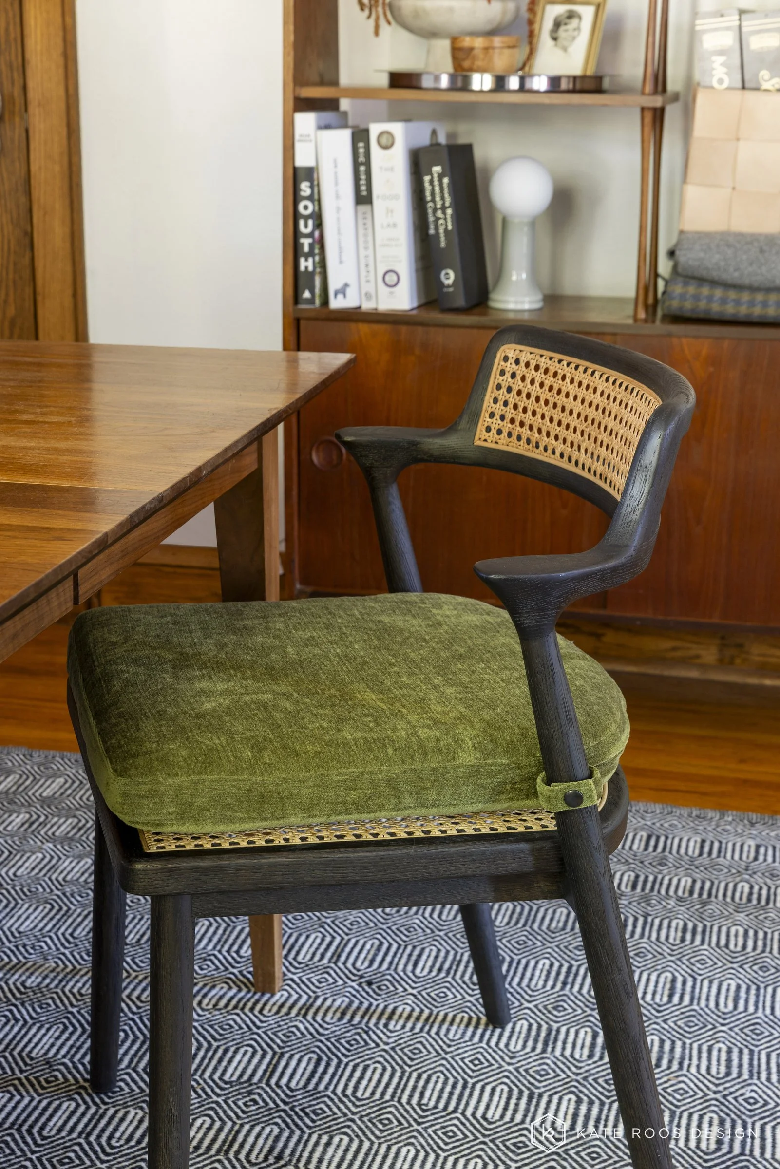 This curated living and dining room showcases a warm modern traditional interior design with strong mid-century modern influences. Original hardwood floors, rich stained wood trim, and a classic arched doorway highlight the home’s historic character 